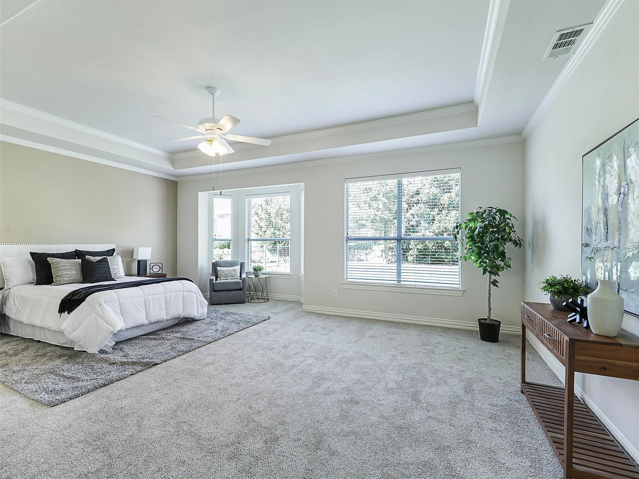 Primary Bedroom with a raised ceiling, multiple windows, ornamental molding, and carpet flooring