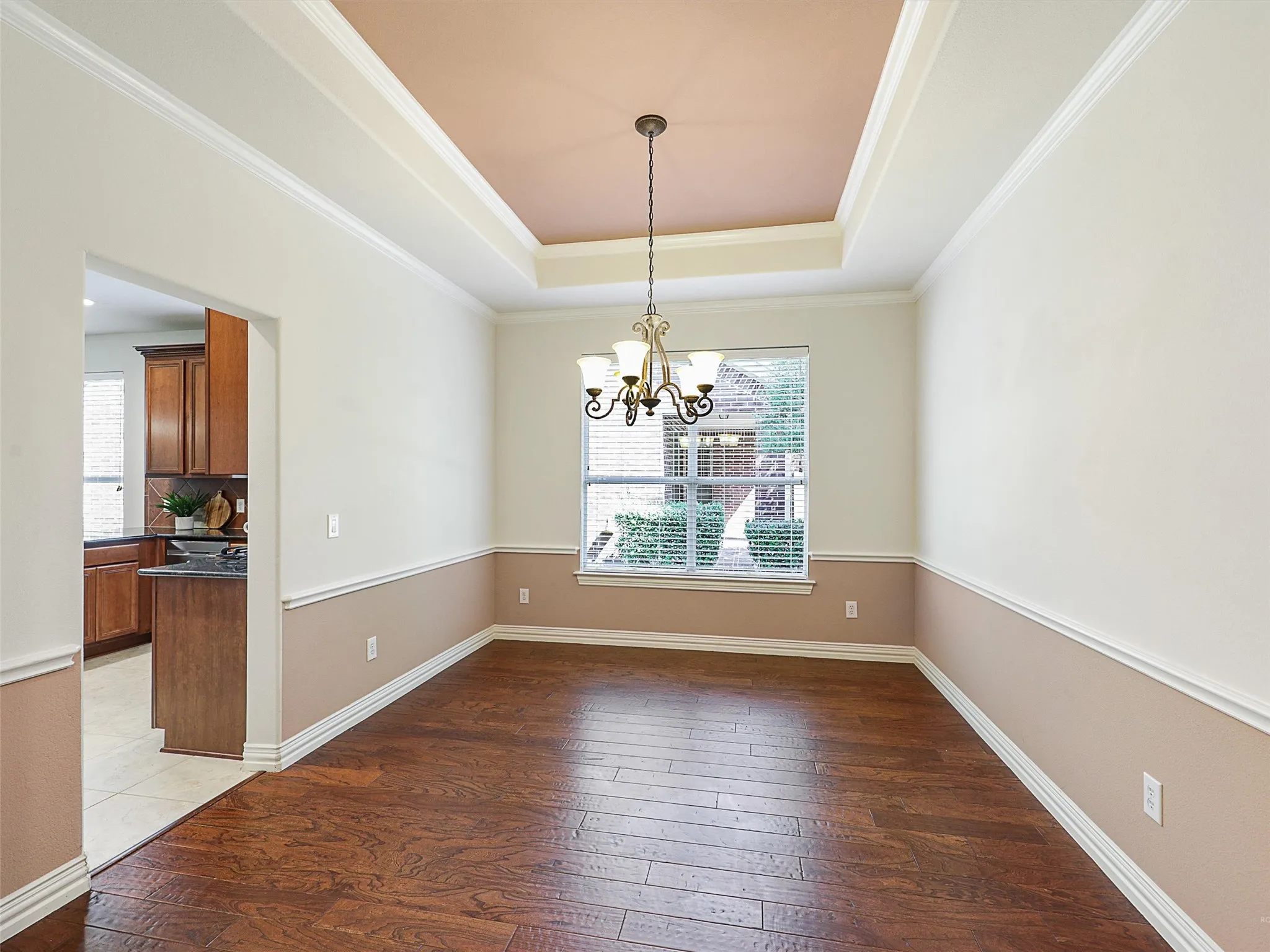 Large dining area with dark wood-type flooring, a tray ceiling, ornamental molding, and a chandelier