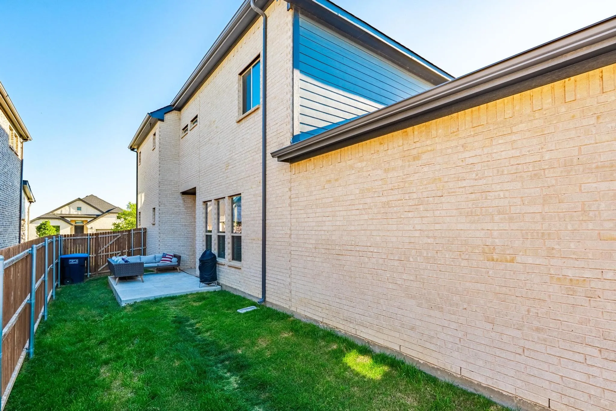 Gated property featuring a brick exterior, well-maintained lawn, and a concrete patio
