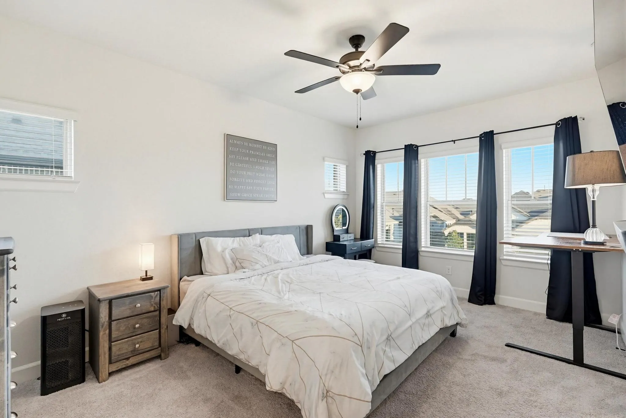 Carpeted bedroom featuring multiple windows, a ceiling fan with integrated lighting, and neutral wall tones