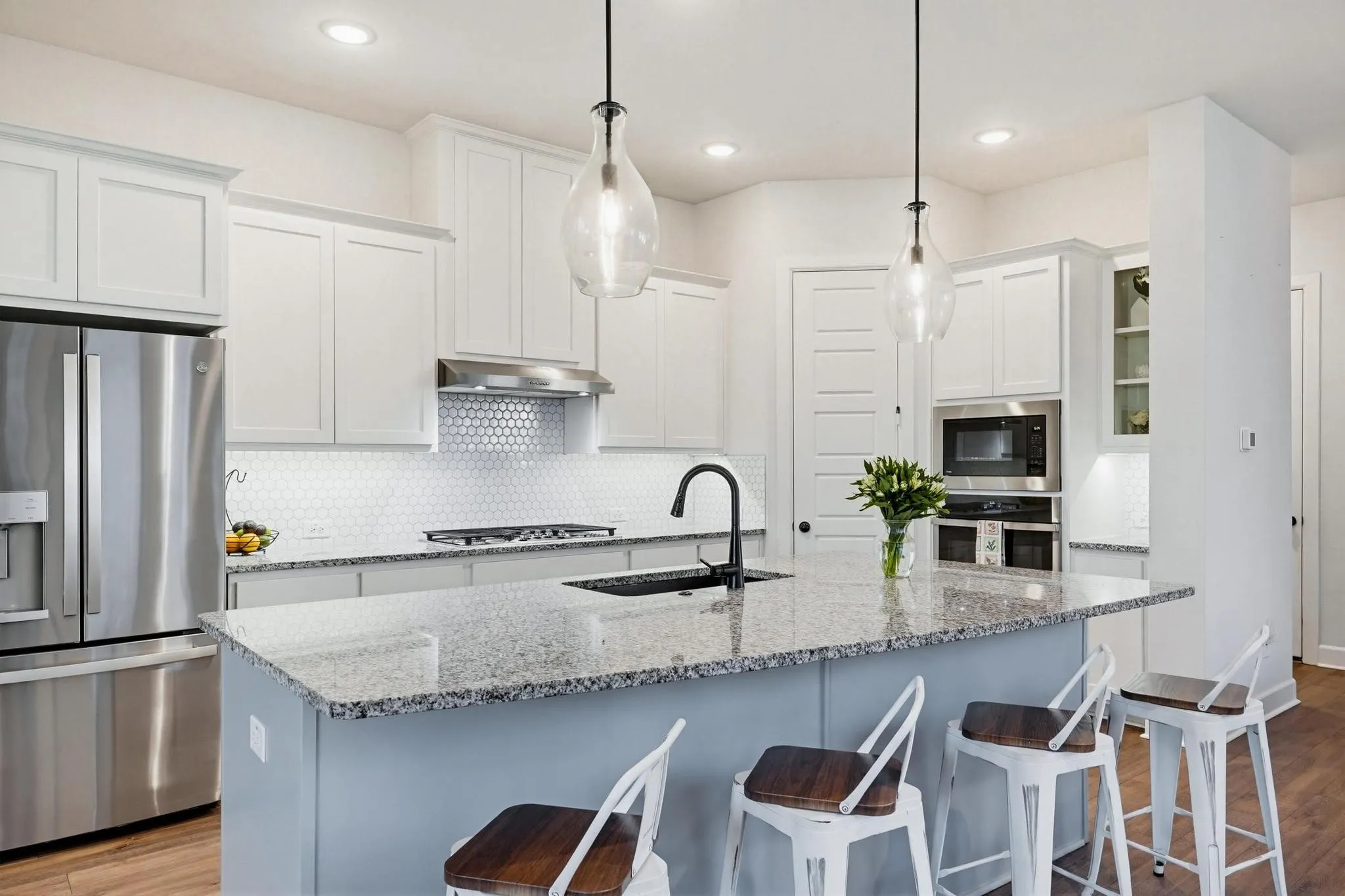 Spacious kitchen featuring an expansive granite island with seating, stainless steel appliances, shaker-style cabinetry, a penny tile backsplash, and wood-finish flooring