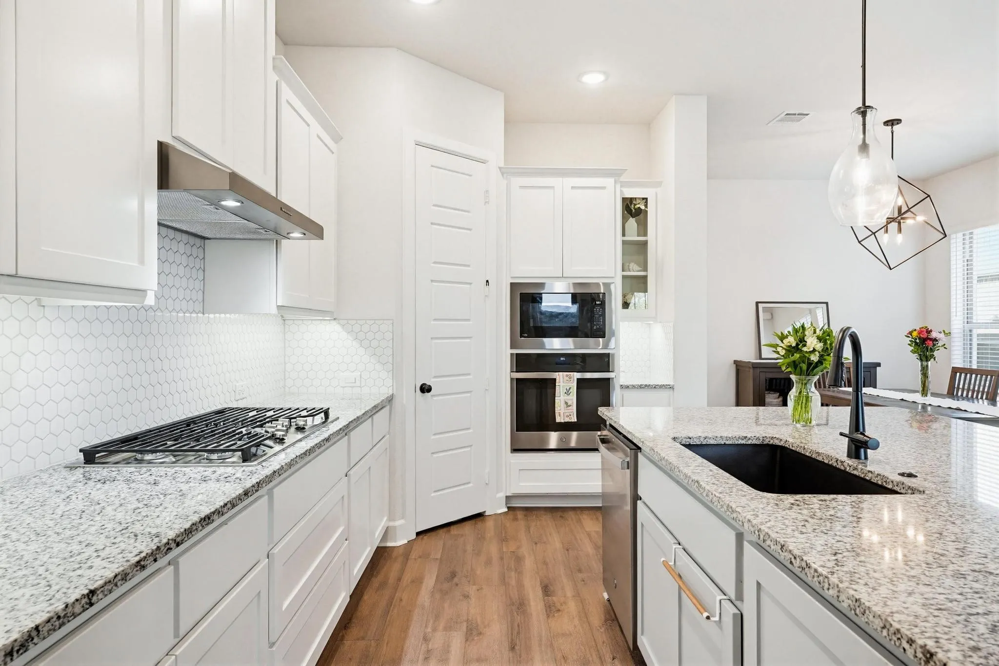 Modern kitchen featuring white cabinetry, granite countertops, a built-in wall oven and microwave, a gas cooktop with an overhead range hood, and a large island with an undermount sink