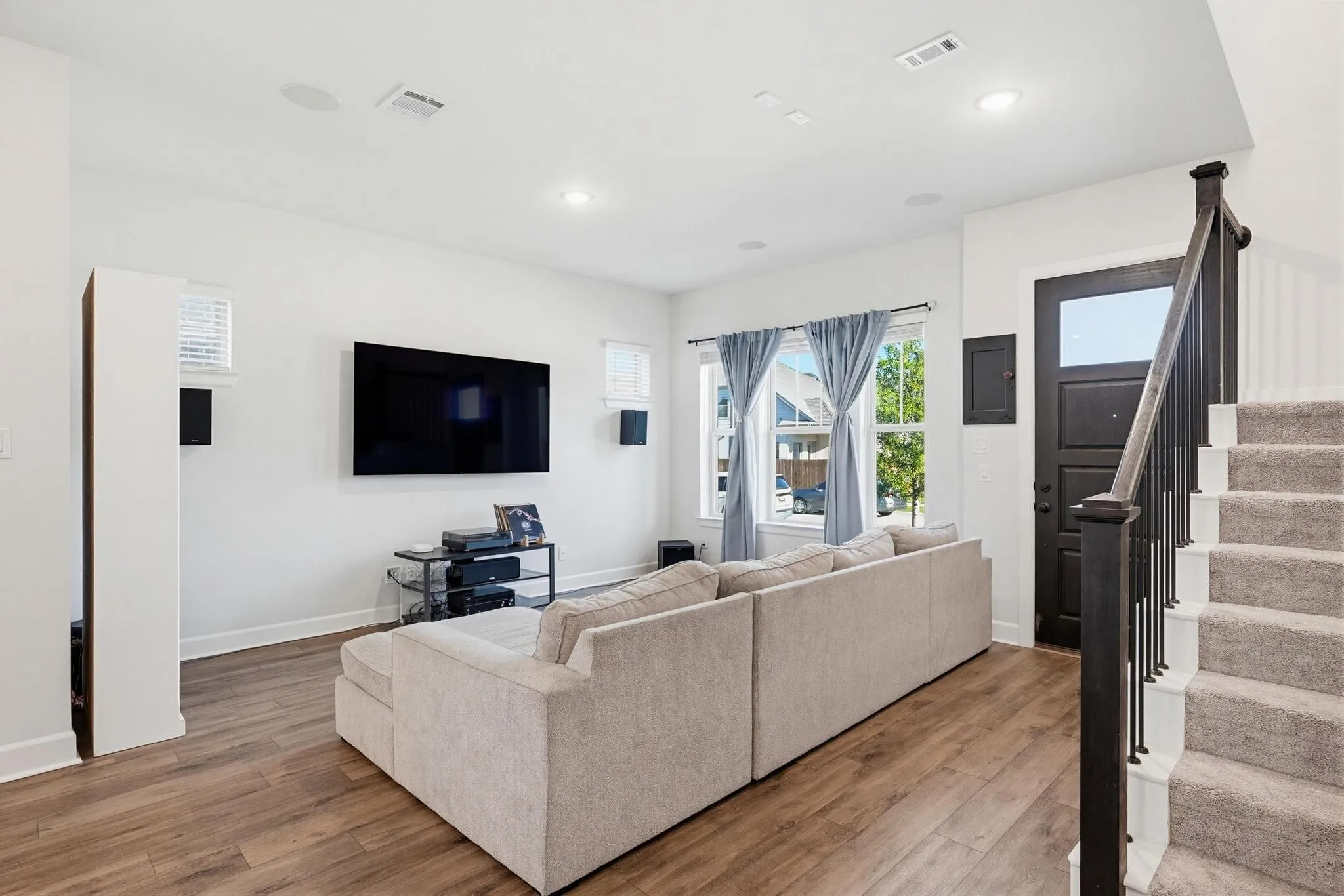 Open-concept living area featuring wood-finish flooring, recessed lighting, and a dark-paneled entry door with an integrated window