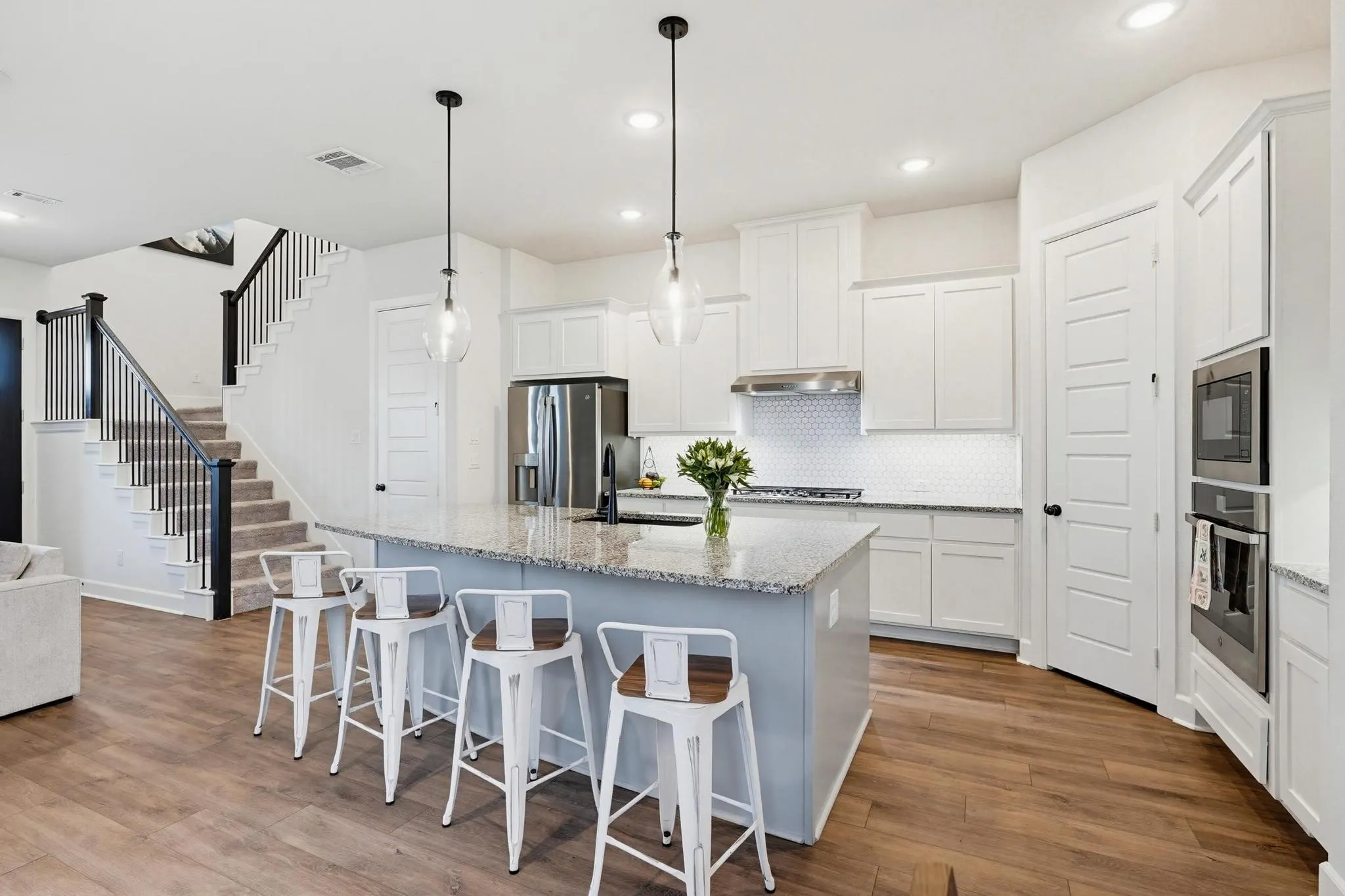 Open-concept kitchen featuring a large island with pendant lighting, stainless steel appliances, white cabinetry, and wood-finish flooring