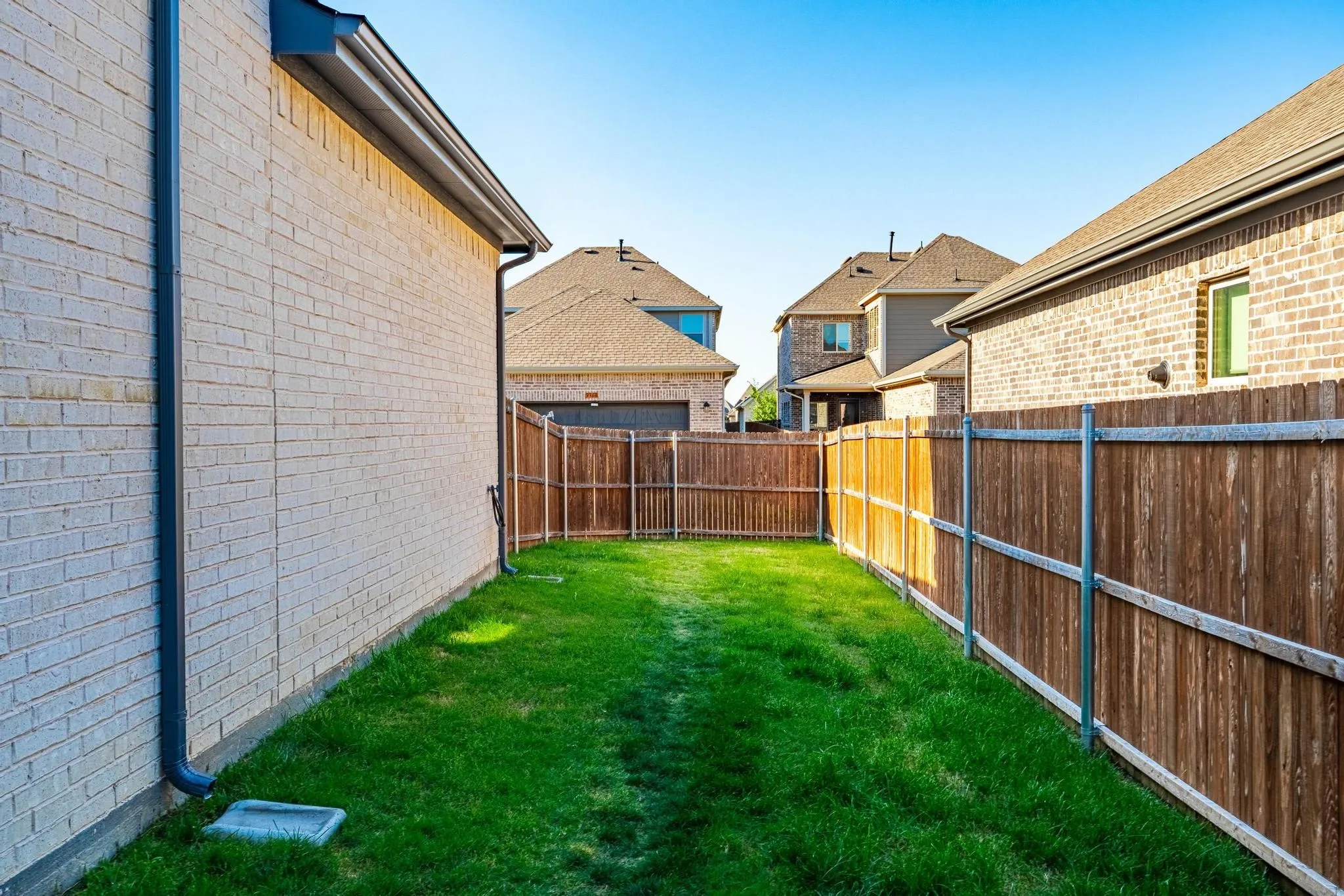 Enclosed backyard featuring a manicured lawn, full privacy fencing, and brick exterior architecture