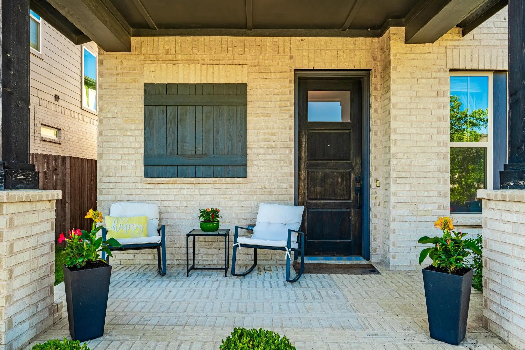 Inviting front porch featuring light-colored brick exterior, dark wood-finish entry door with glass paneling, and a brick paver patio