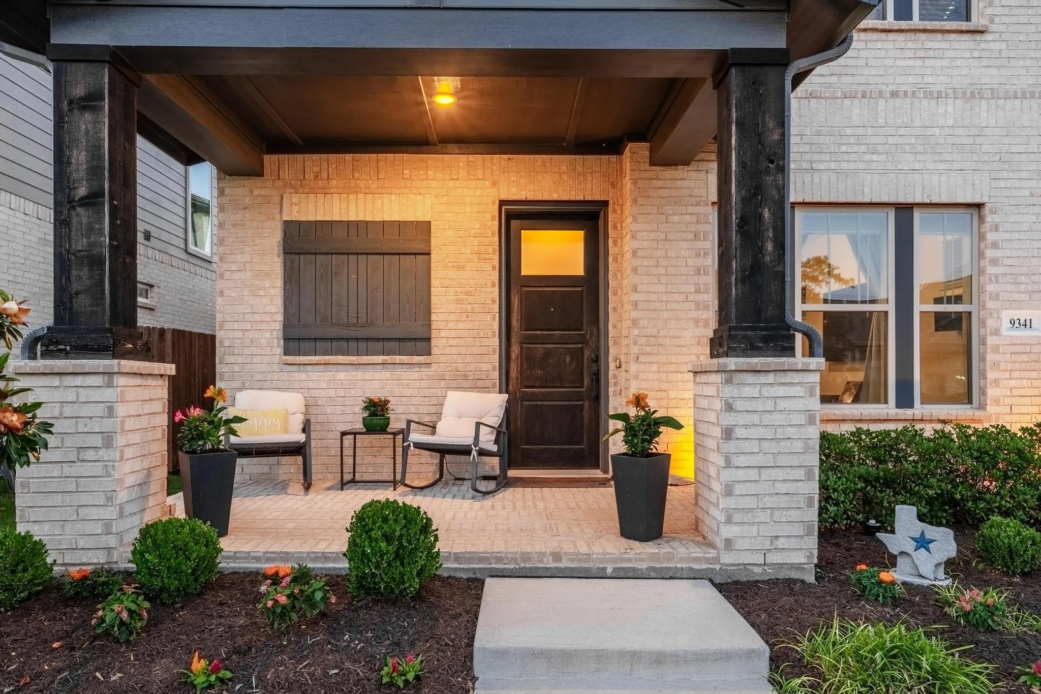 Covered brick porch featuring dark wood-finish columns, a solid wood-finish entry door with clear glass panels, and horizontal wood shutters