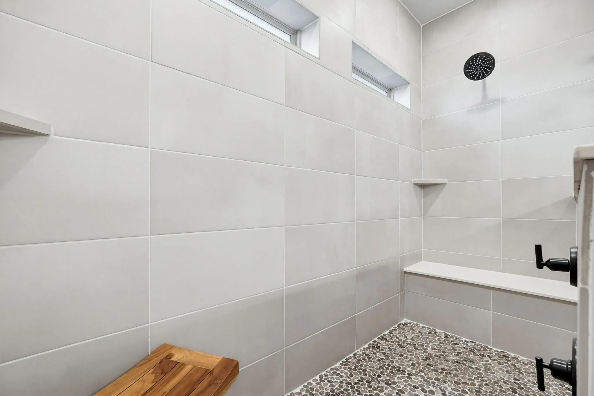 Tiled shower with pebble flooring, integrated bench seating, built-in shelf, and transom windows