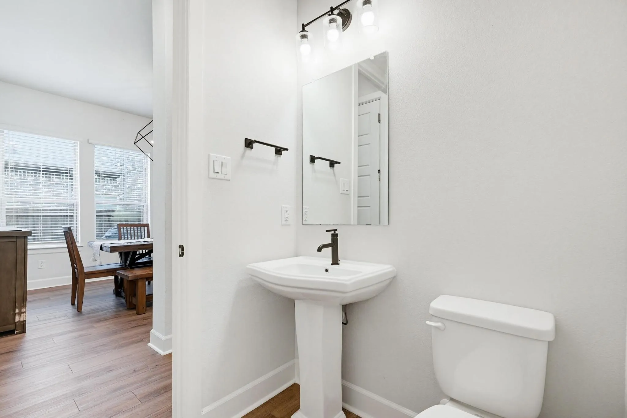 Pedestal sink with a matte black faucet, wall-mounted mirror, and vanity lighting fixture