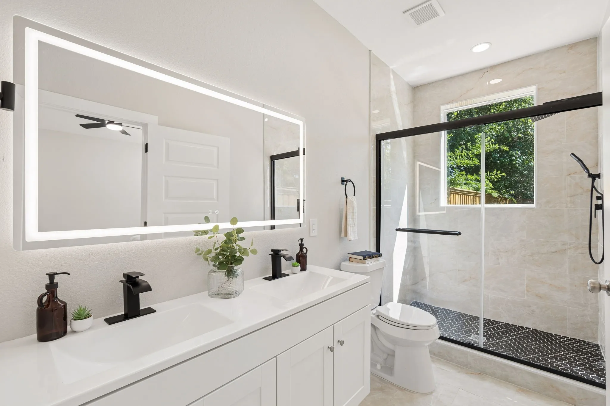 Dual vanity with integrated sinks and black matte fixtures, illuminated by a large back-lit mirror