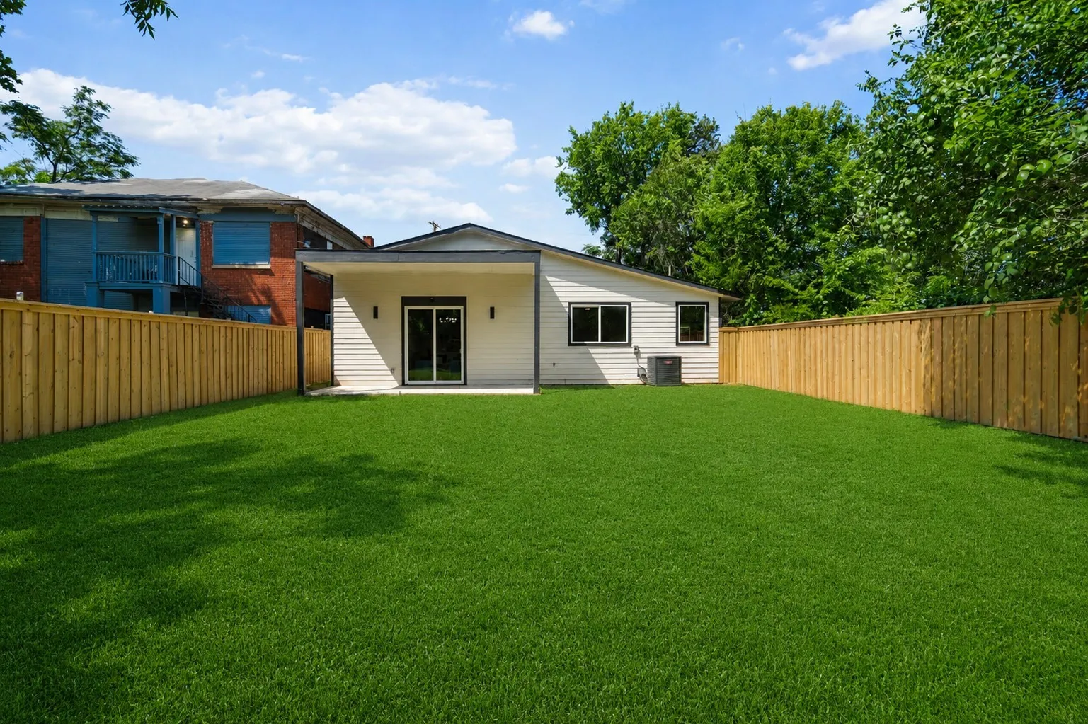 Expansive backyard featuring a manicured lawn, a newly installed wood privacy fence, and a modern exterior with sliding glass doors