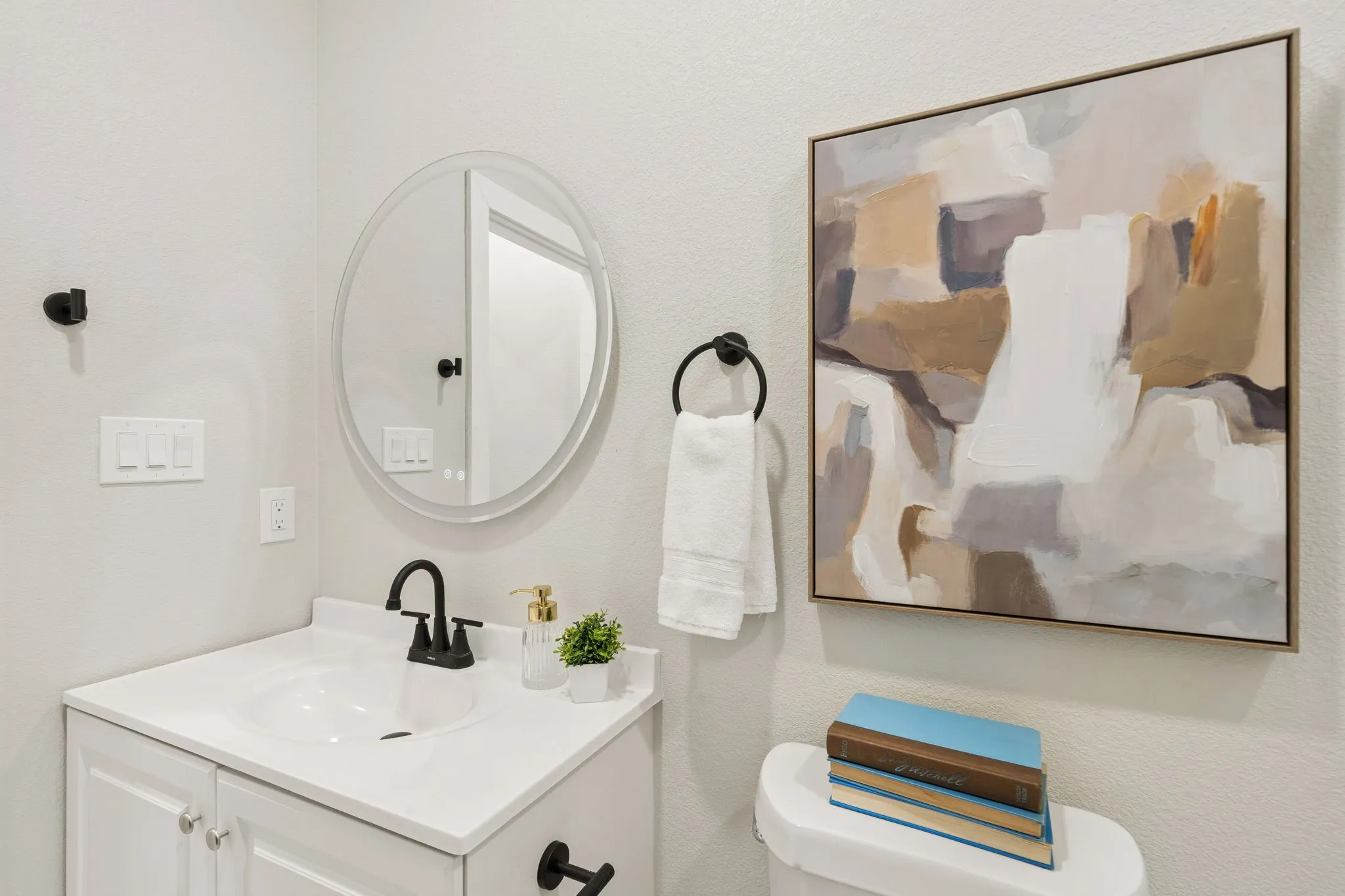 Bathroom featuring a white vanity with integrated sink, black hardware, an oval-shaped mirror, and light-toned walls