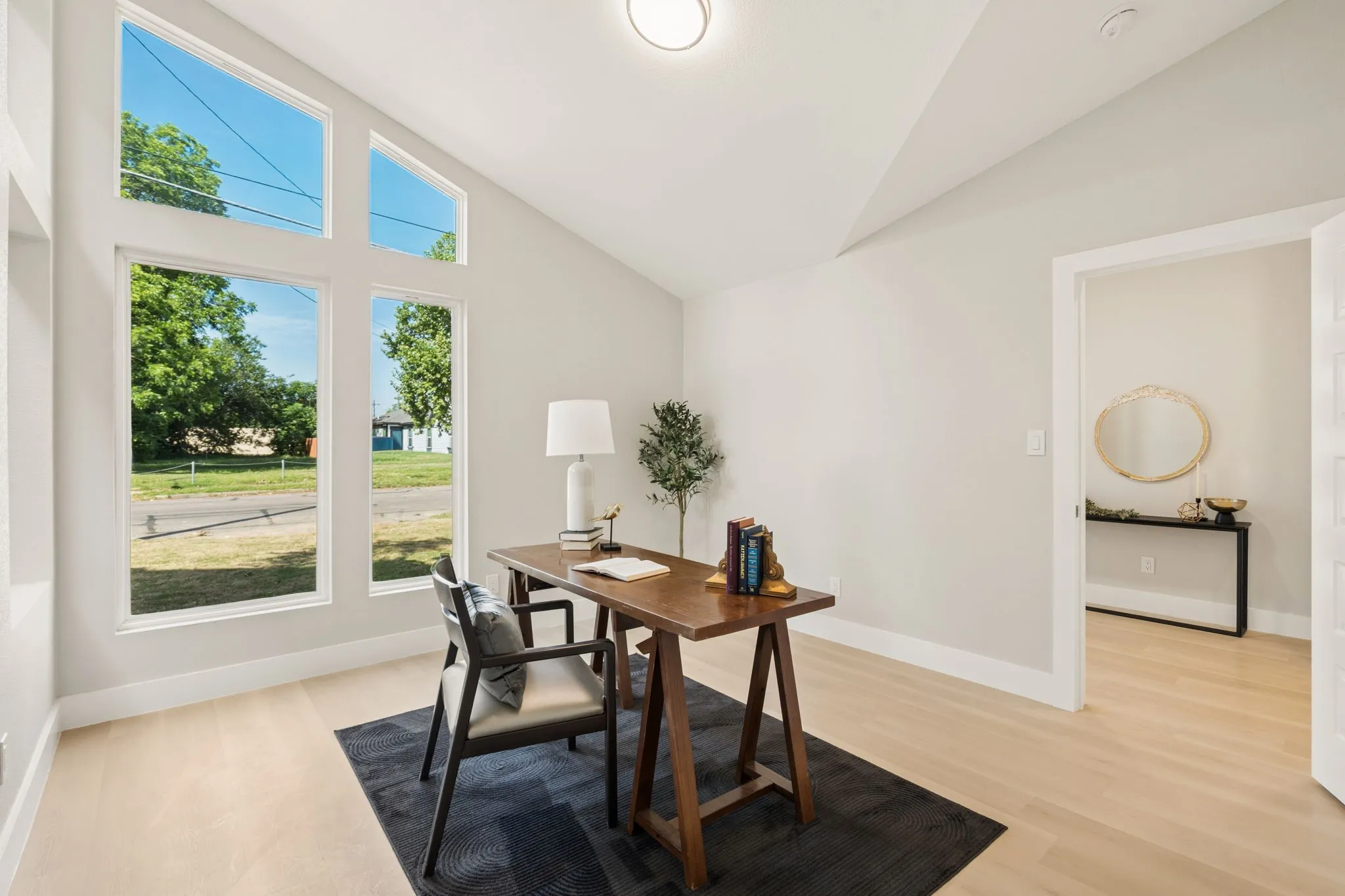 Vaulted ceiling interior space featuring a large window array, wood-finish flooring, and light neutral wall paint