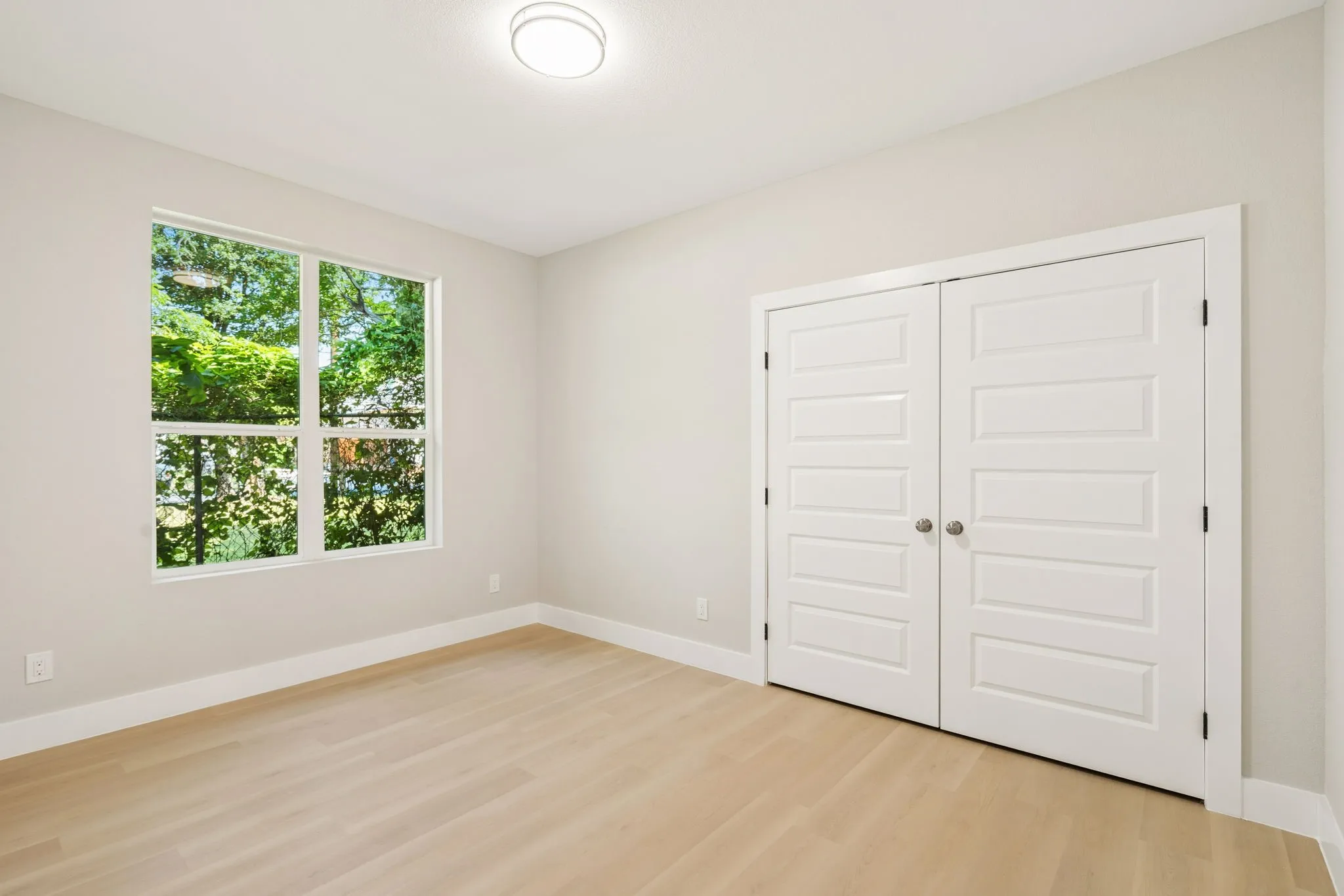 Bright room featuring a large window, light-toned wood-finish flooring, white baseboards, and a flush mount ceiling light