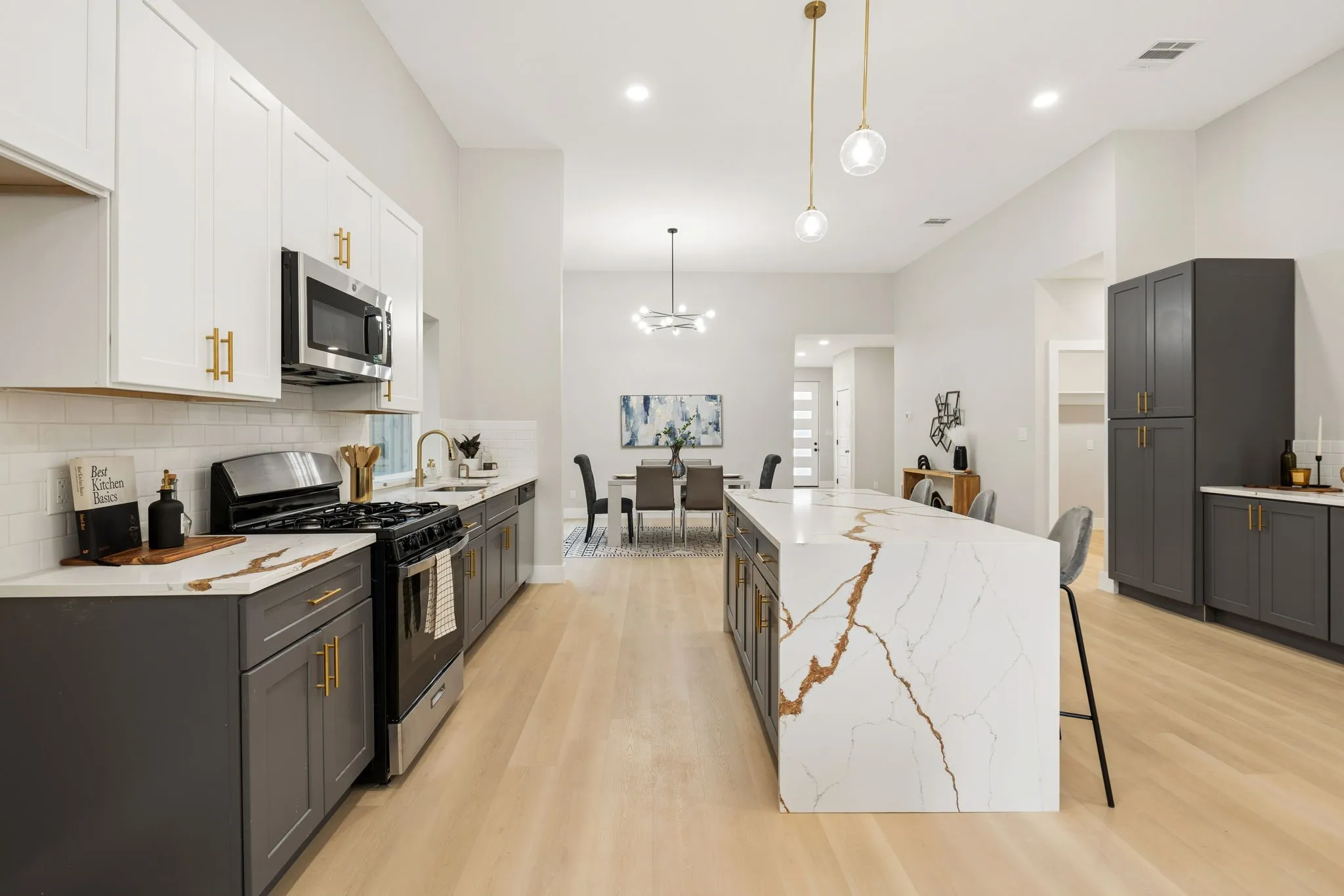Open-concept kitchen with a large waterfall island featuring distinctive veining, light wood-finish flooring, and recessed lighting