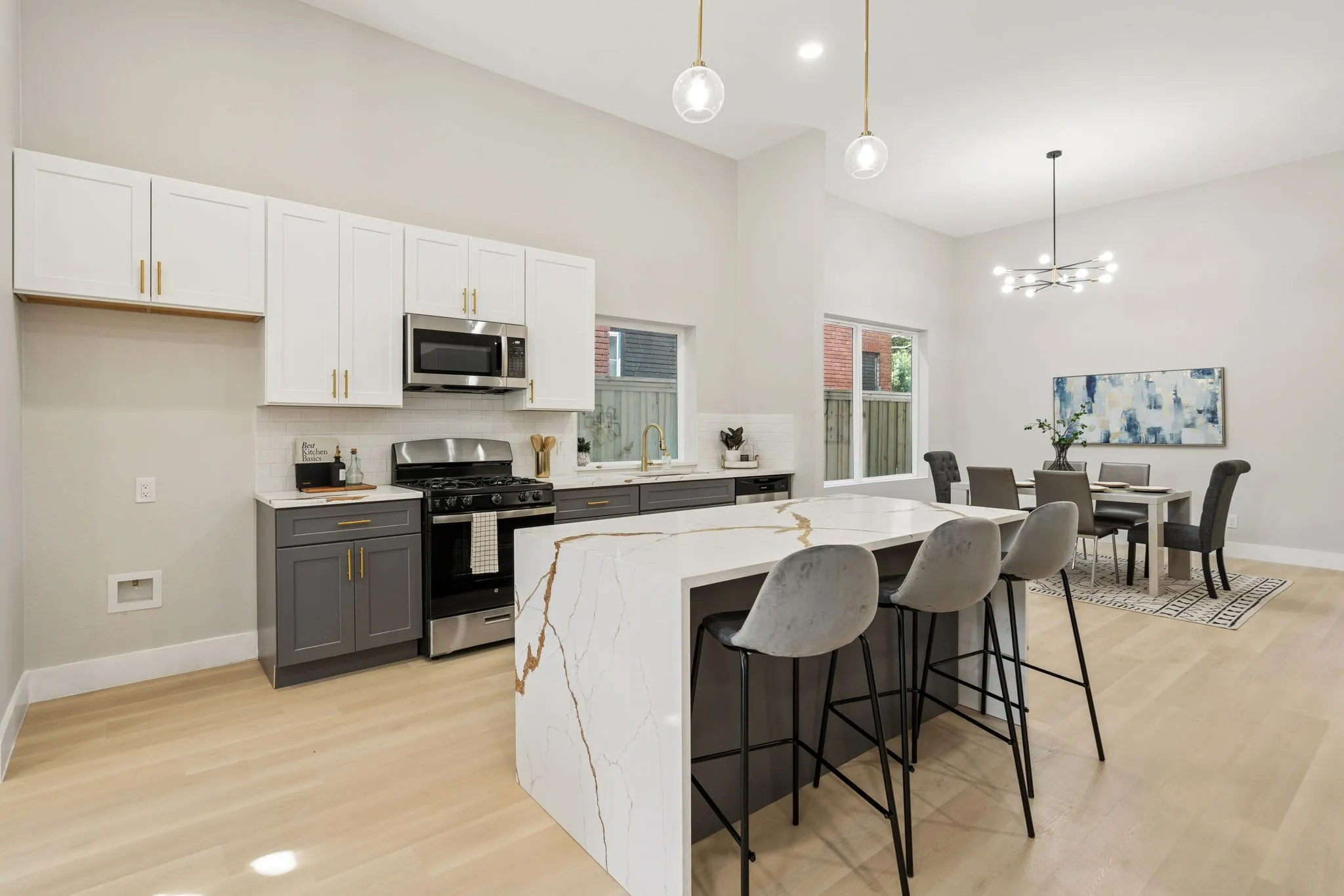 Open-concept kitchen featuring a waterfall island with a stone-finish countertop, two-tone cabinetry, stainless steel appliances, and light wood-finish flooring