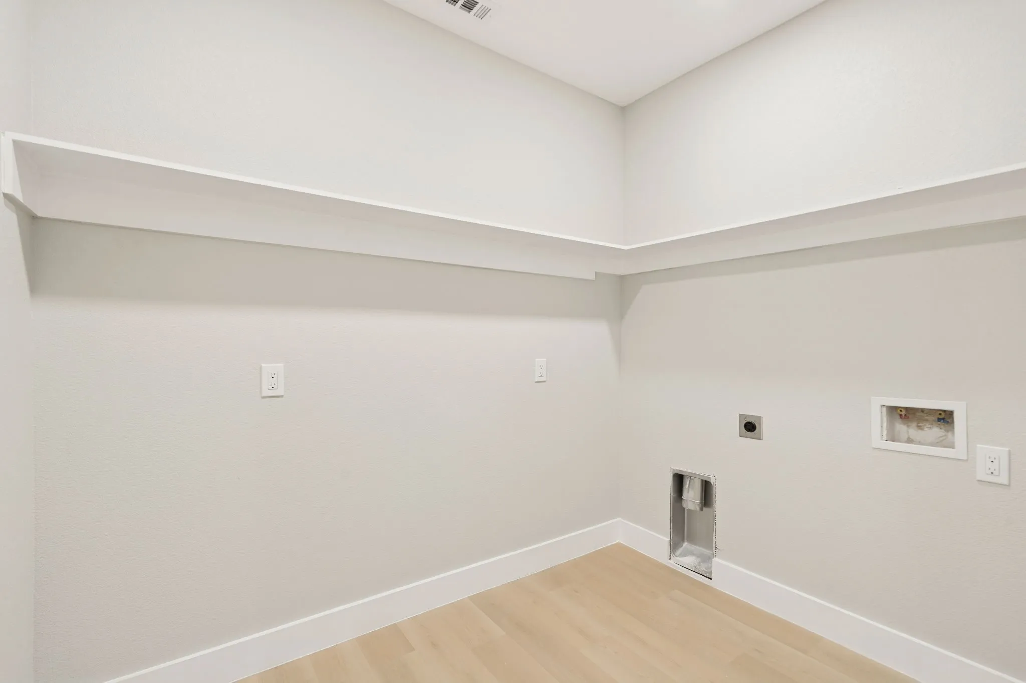 Dedicated laundry area featuring light wood-finish flooring, white baseboards, and built-in shelving