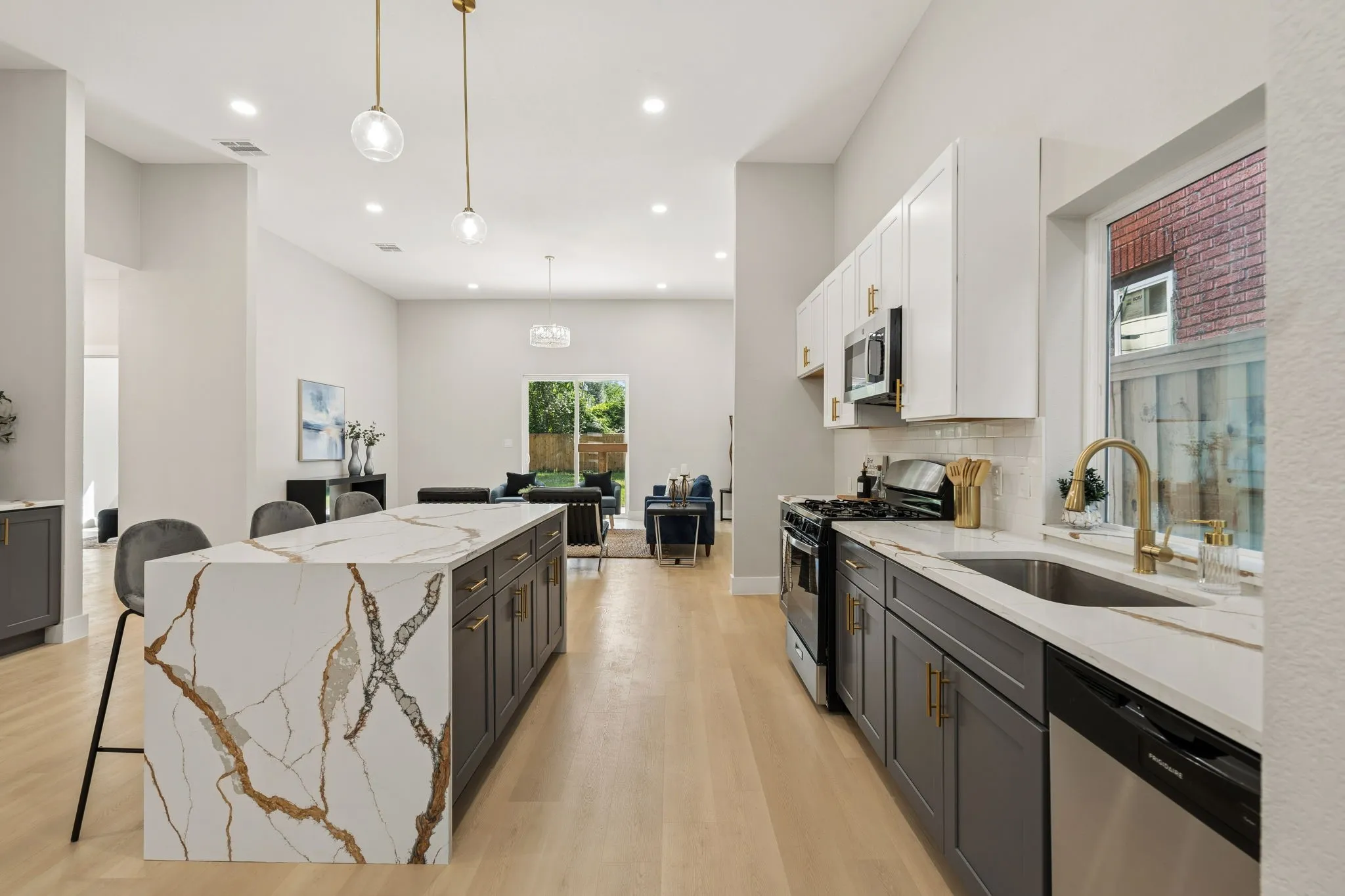 Contemporary kitchen featuring a waterfall island with a patterned stone countertop, two-tone cabinetry, stainless steel appliances, and wood-finish flooring