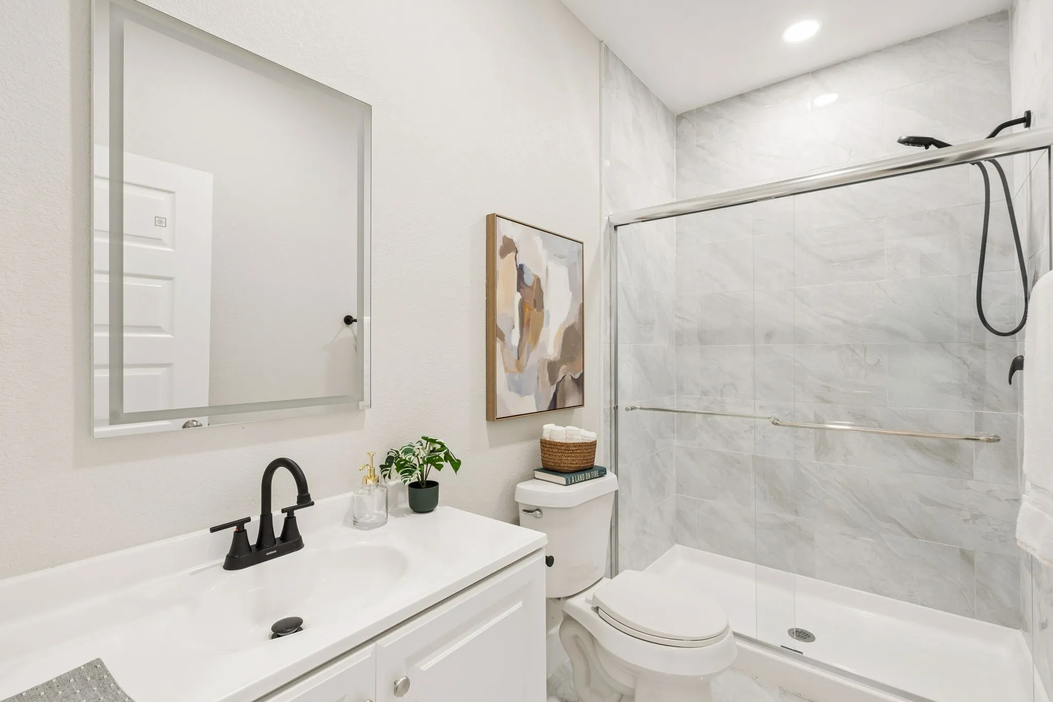 Contemporary bathroom featuring a white vanity with integrated sink, matte black faucet, and a large illuminated mirror