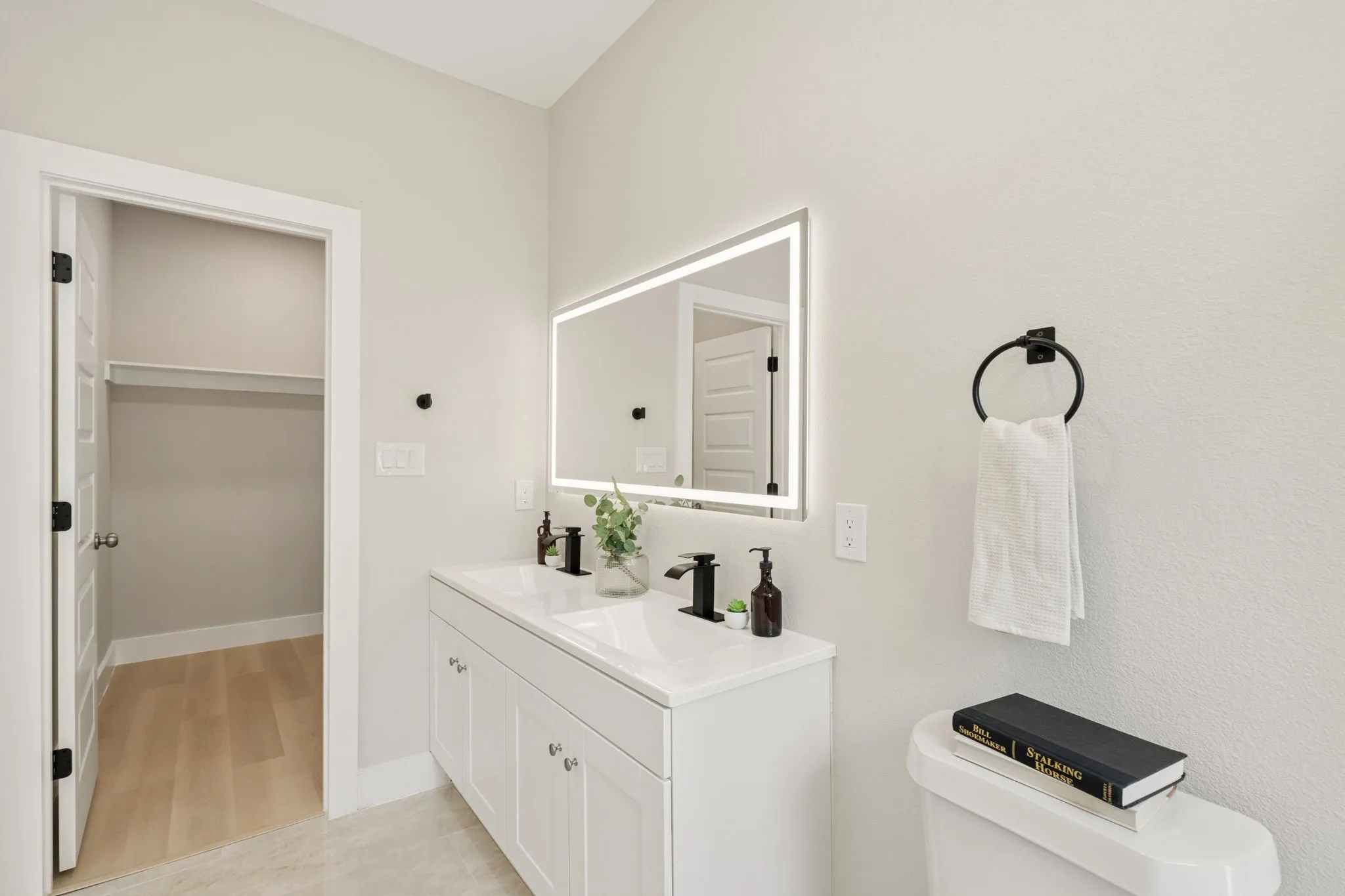 White double vanity with integrated sinks and matte black fixtures, illuminated by a backlit mirror