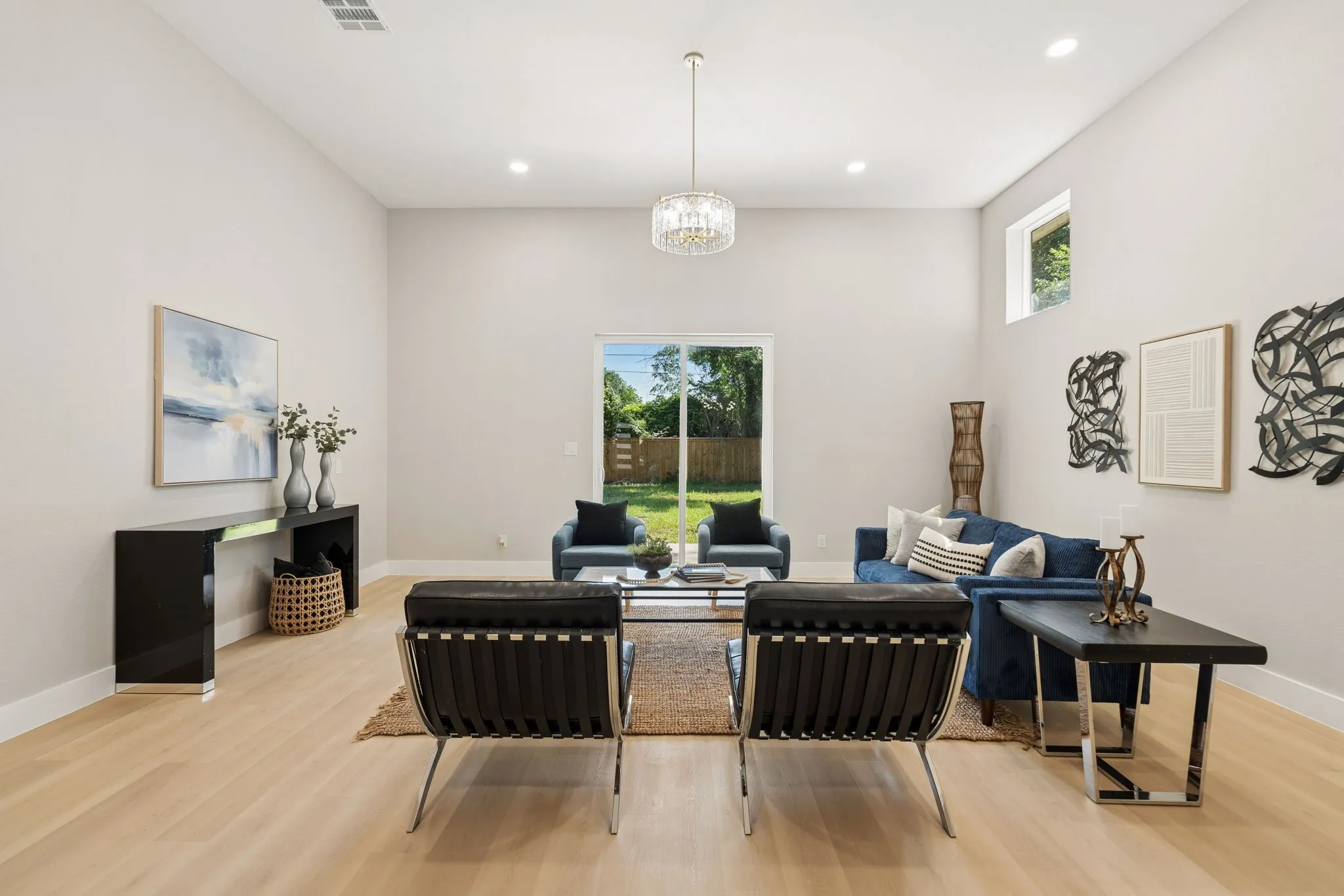 Spacious living area featuring light wood-finish flooring, high ceilings, recessed lighting, and a modern chandelier