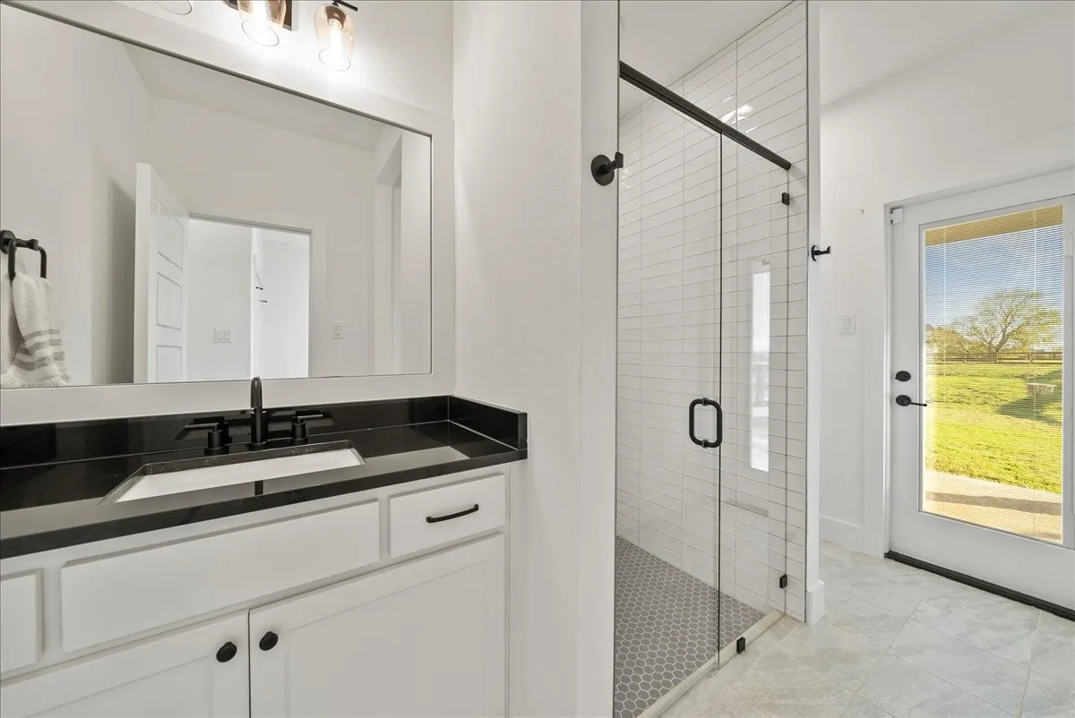 Secondary Primary Bathroom with Full Ensuite, Curbless Walk-in Shower, Built-in Cabinets, Natural Stone Countertop, and Exterior Door leading to Rear Patio