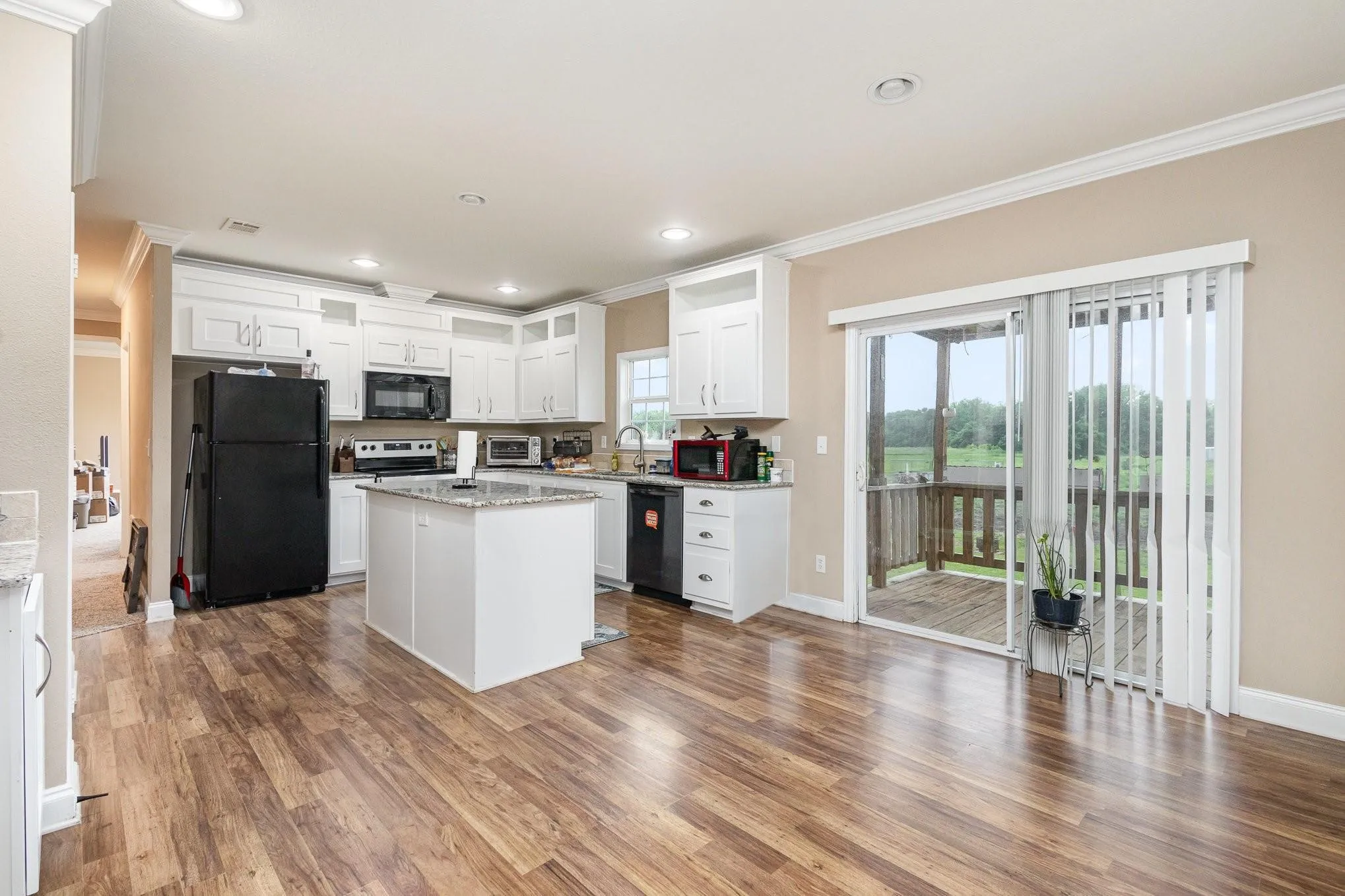 Kitchen featuring white cabinetry, wood-finish flooring, a central island with a stone countertop, and sliding glass doors opening to a deck