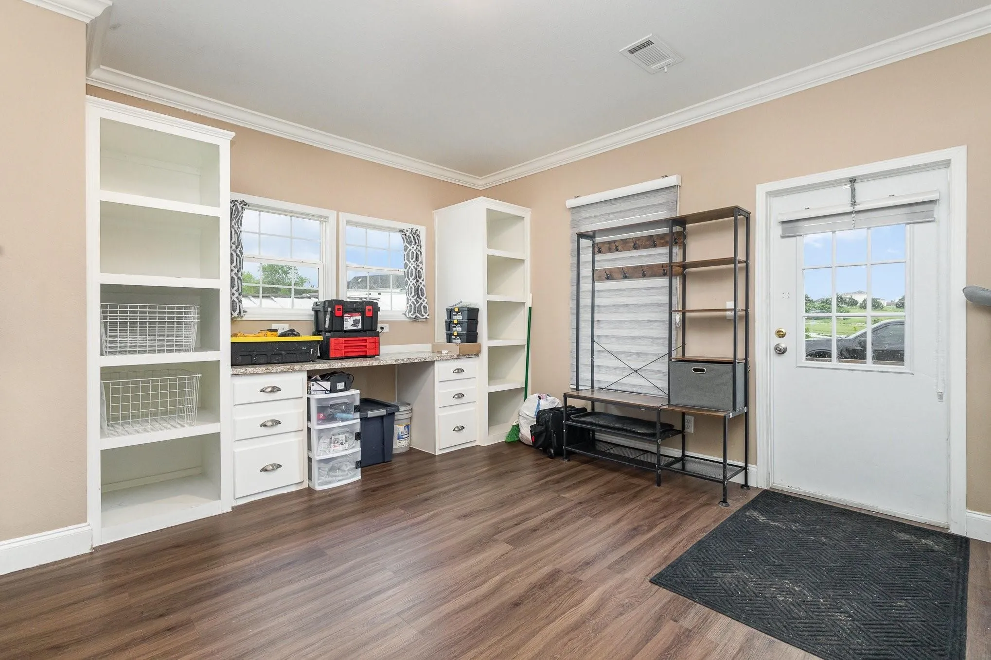 Spacious utility area featuring wood-finish flooring, two large windows, white built-in shelving, a built-in desk with drawers, and a white exterior door with window panes