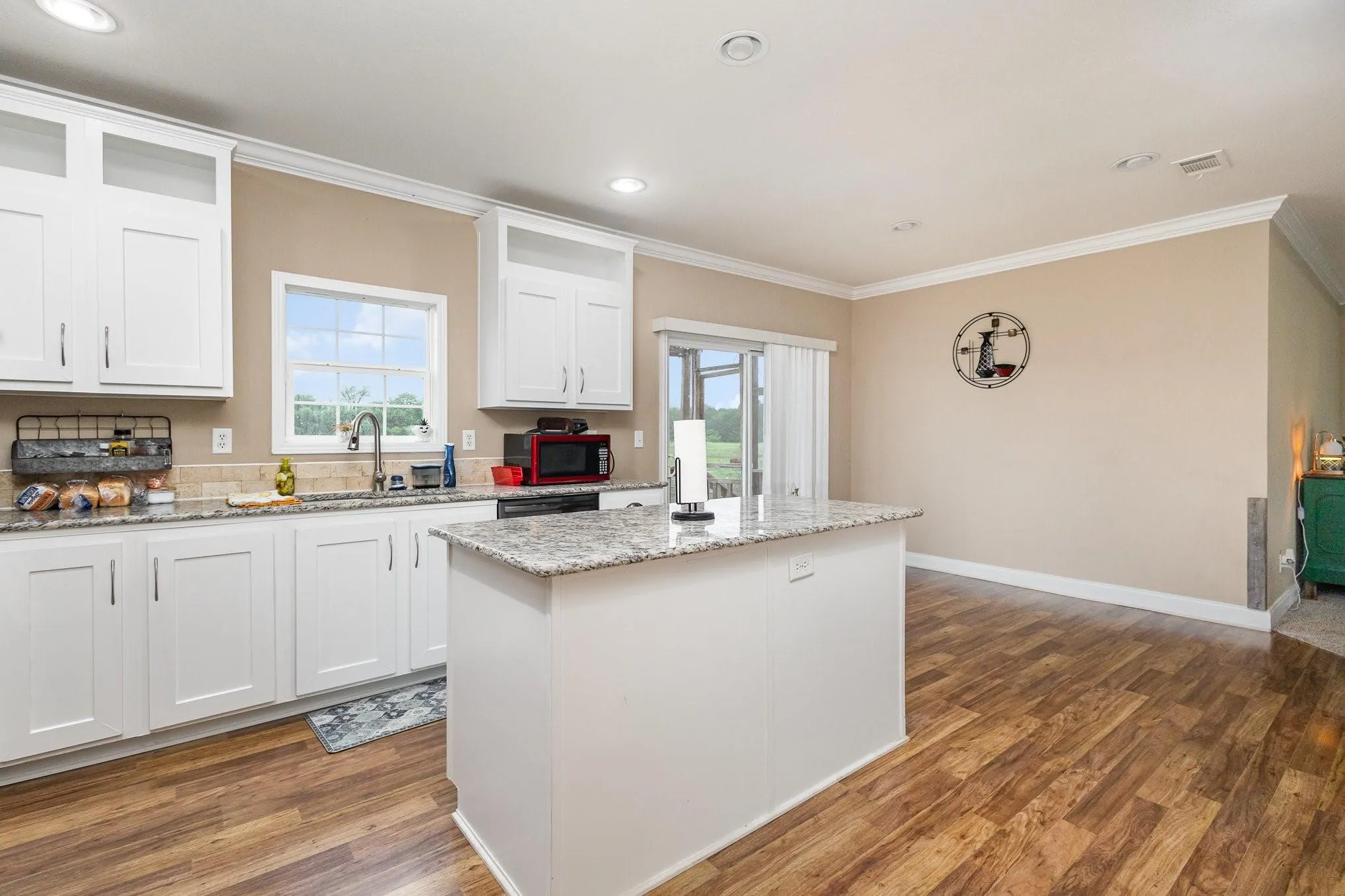 Kitchen featuring white shaker-style cabinetry, a central island with a granite-style countertop, and wood-finish flooring