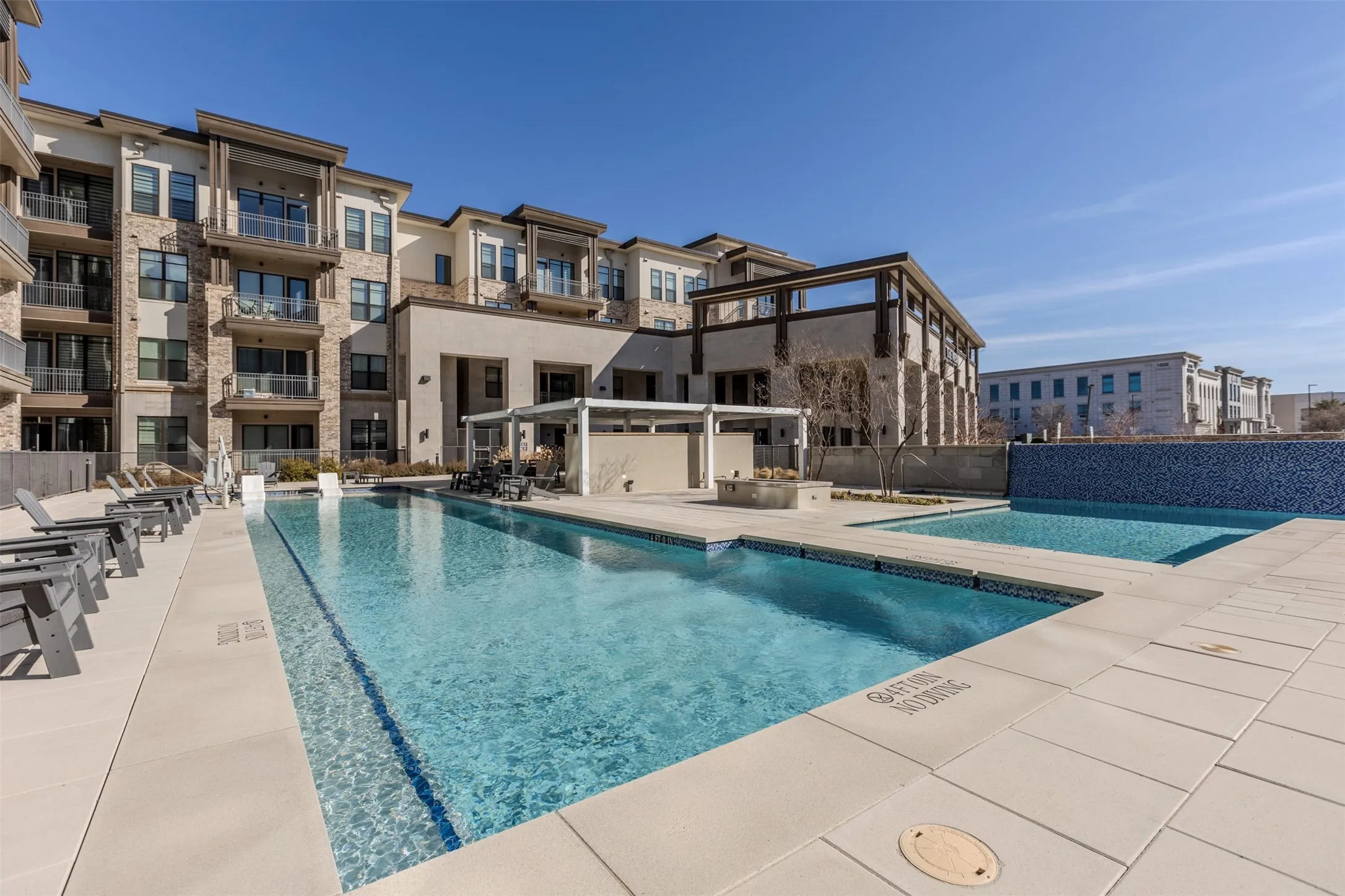 Outdoor aquatic area featuring a large swimming pool, a secondary shallow pool, and a tiled water feature