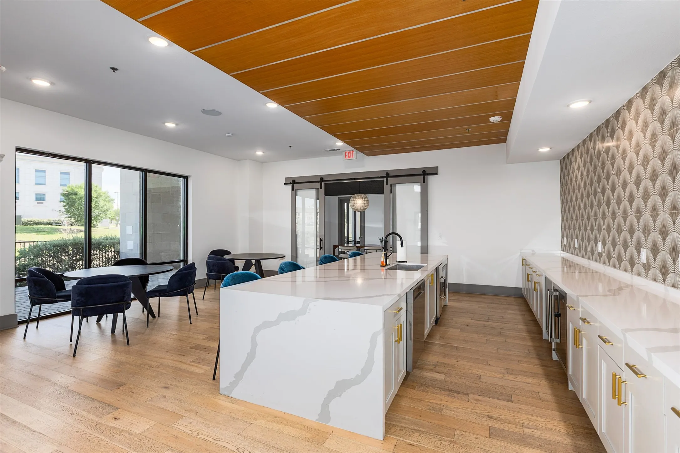 Spacious common area featuring an expansive stone-finish island with integrated sink, wood-finish flooring, and floor-to-ceiling windows