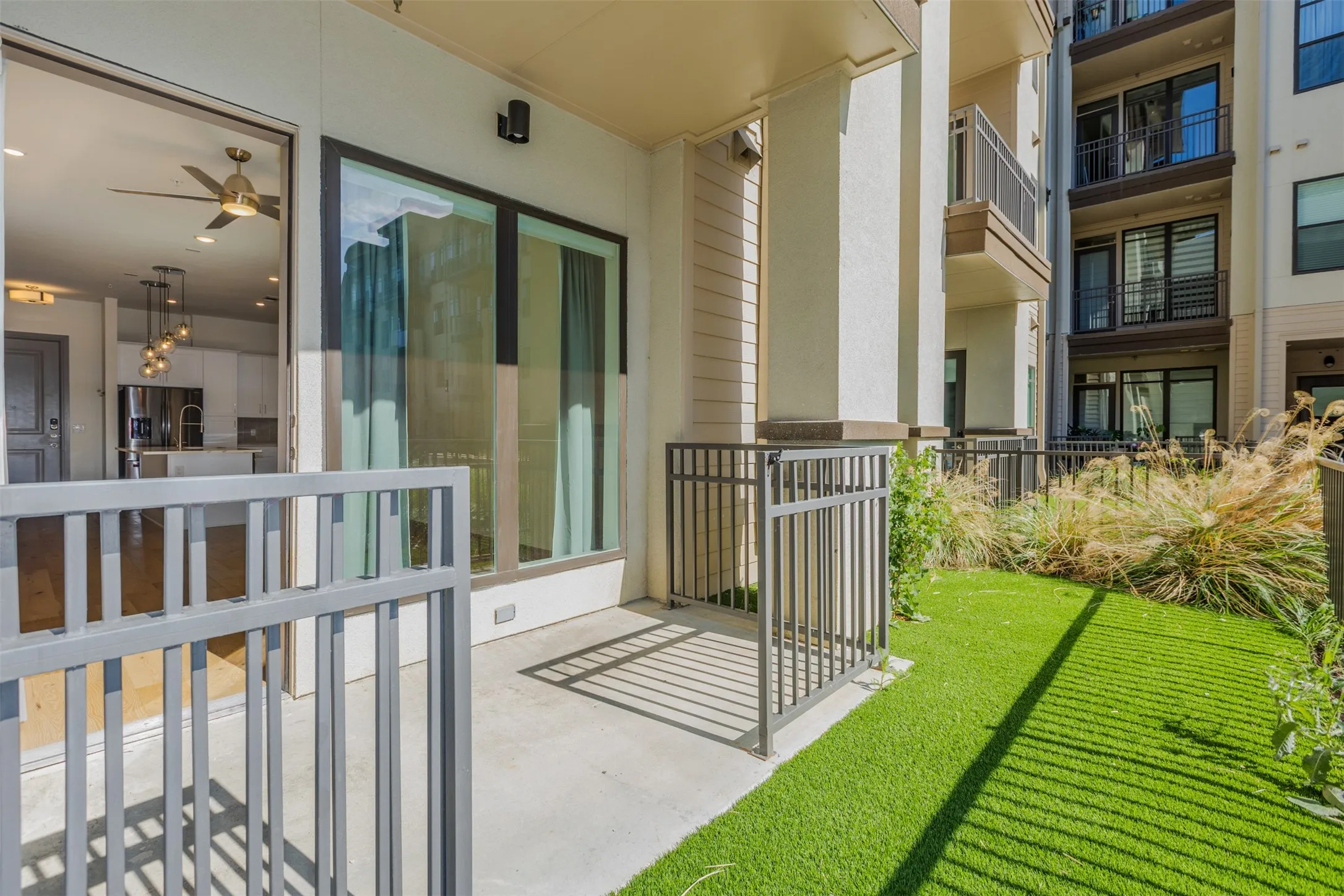 Ground-level patio featuring artificial turf, metal railings, and natural landscaping