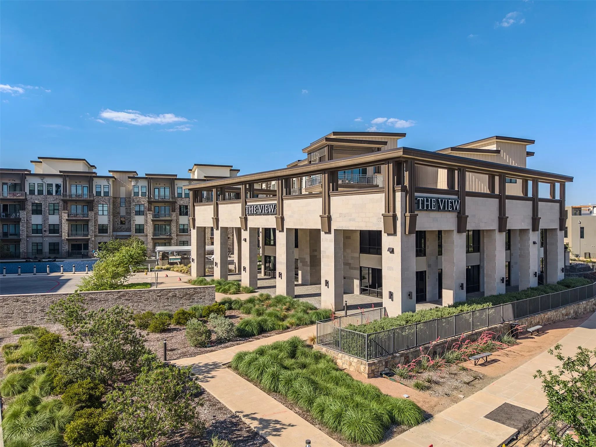 Modern multi-story building featuring a prominent "The View" sign, stone-clad pillars, expansive windows, and a structured outdoor landscaping with pathways and various plantings