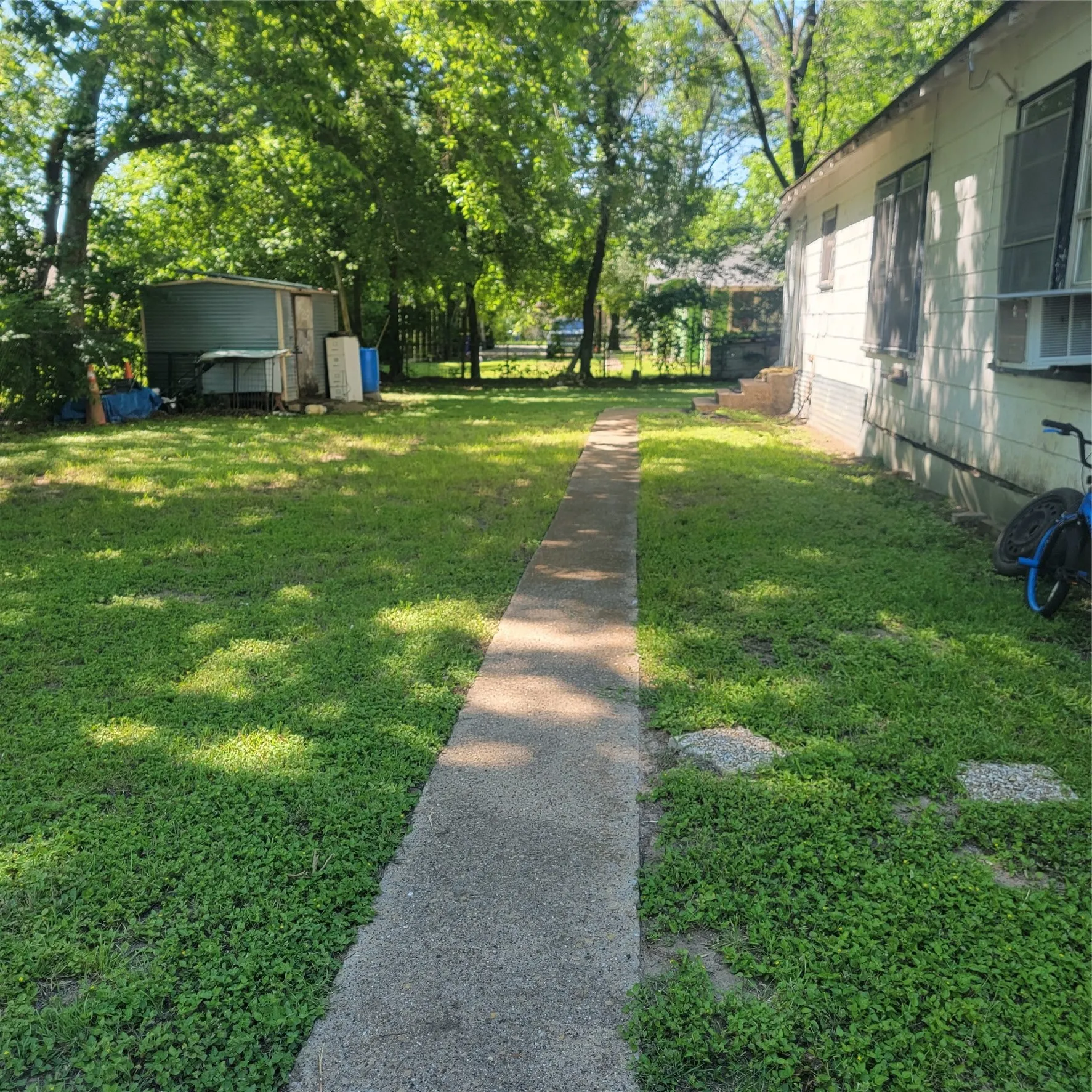 Spacious rear yard with a concrete pathway and mature trees providing natural shade