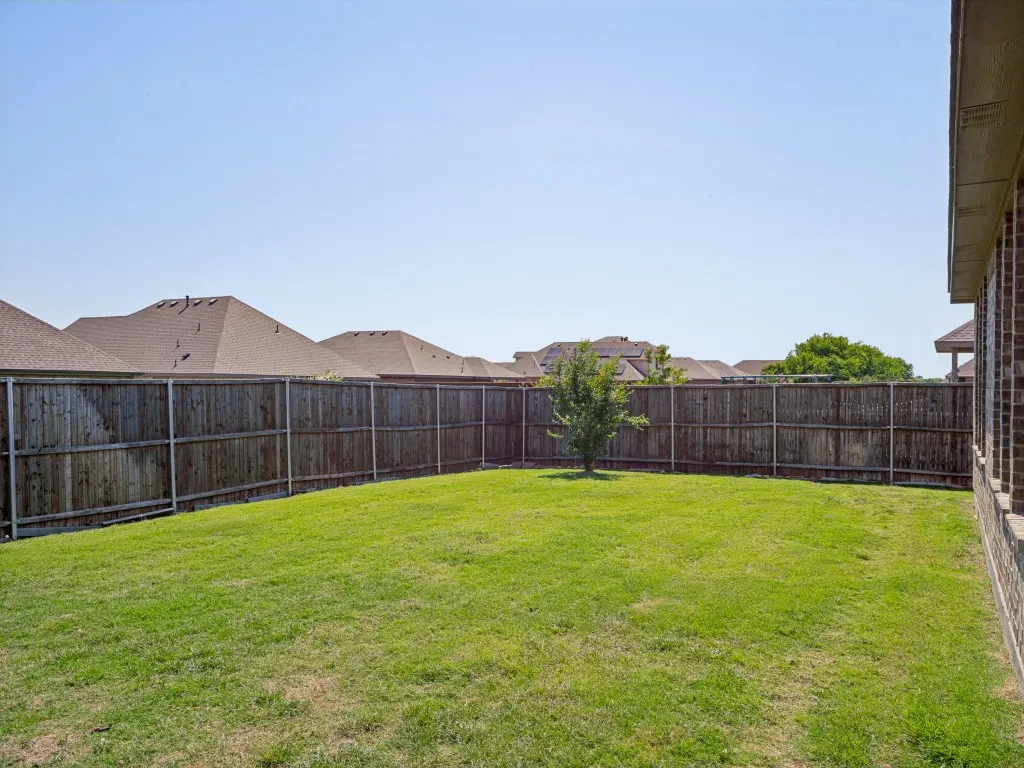 Expansive backyard with a manicured lawn, full privacy fencing, brick exterior wall, and a single mature tree