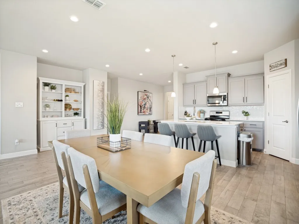 Open-concept living area featuring wood-finish flooring, recessed lighting, a built-in kitchen island with pendant lighting, light gray cabinetry, and stainless steel appliances