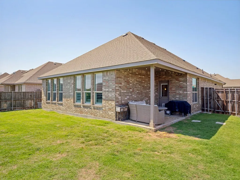 Rear exterior featuring a covered patio with brick paving, multiple windows with interior plantation shutters, and a shingled roof
