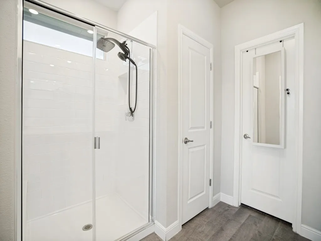 Walk-in shower featuring a sliding glass door, white subway tile surround, and a rain shower head with an additional handheld sprayer