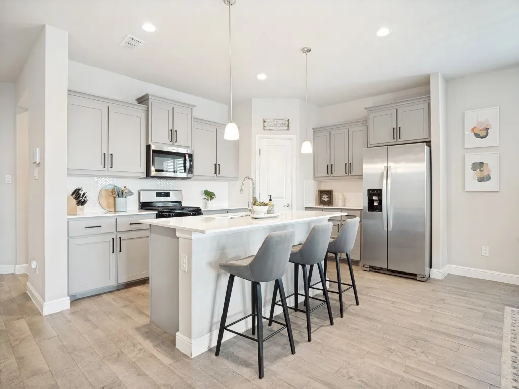 Contemporary kitchen featuring a central island with countertop seating, light gray cabinetry, stainless steel appliances, a herringbone tile backsplash, and wood-finish flooring