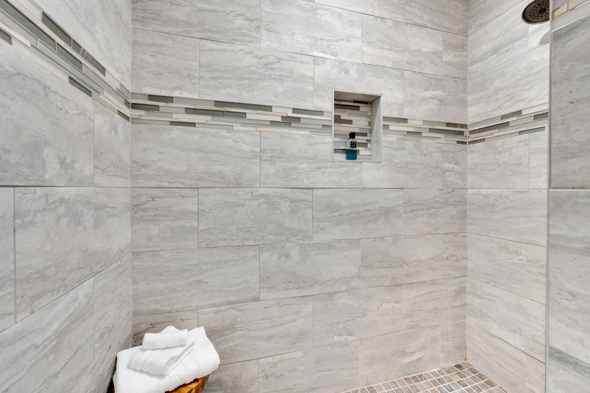 Beautifully tiled walk-in shower with a decorative accent band in the primary bath.