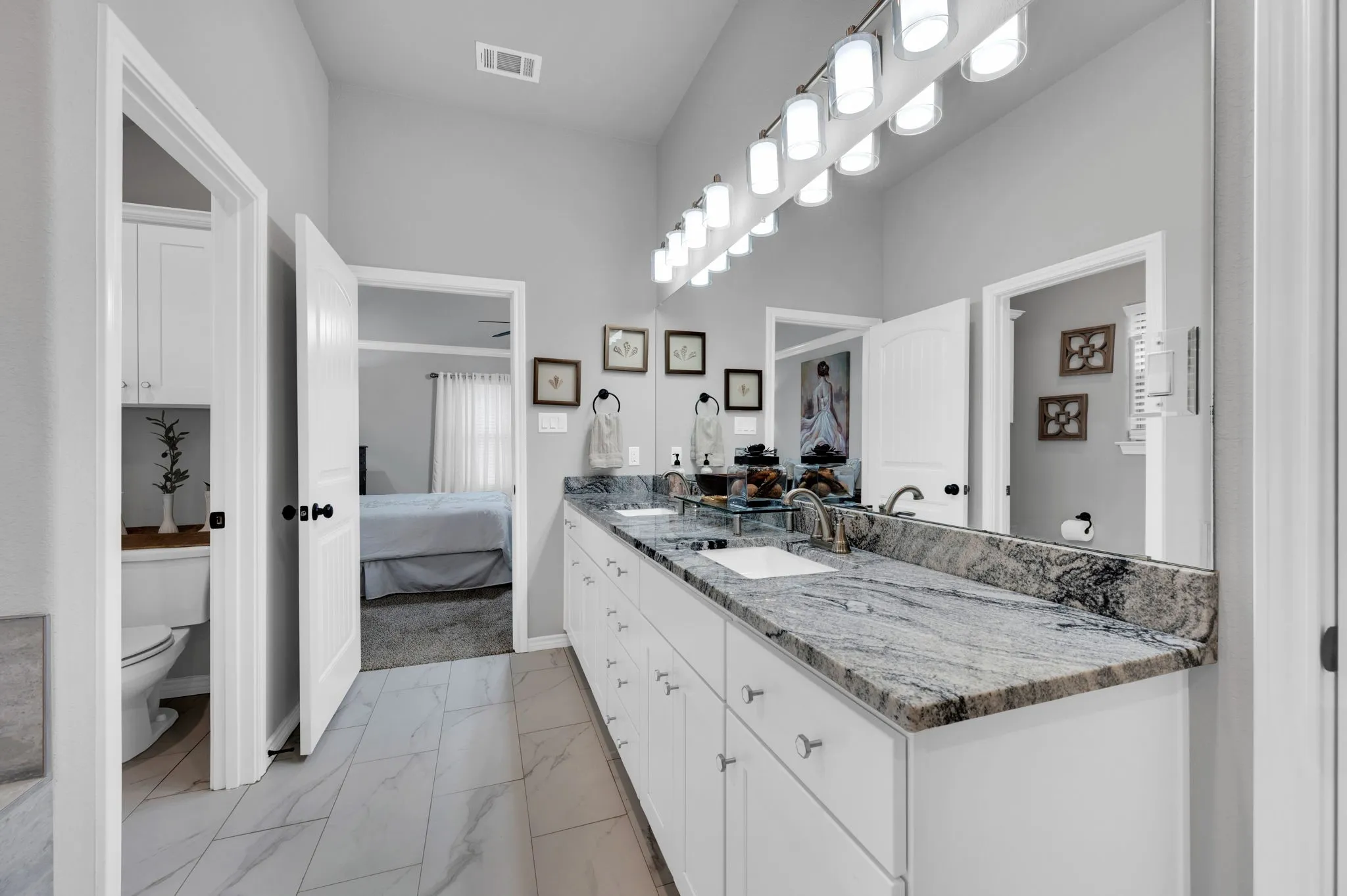 Spa-like primary bath featuring a granite double vanity and a view into the bedroom suite.