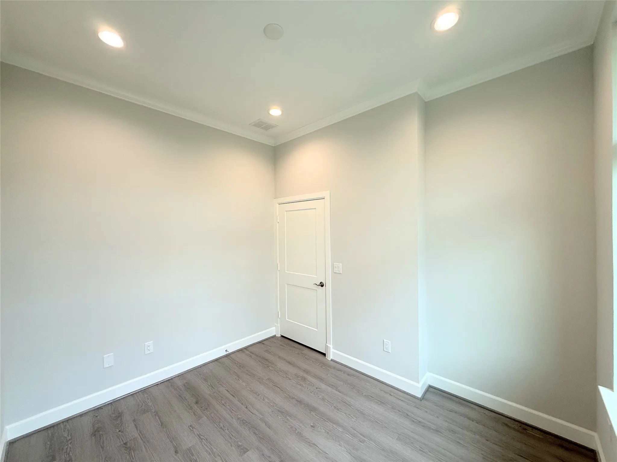 Interior room with wood-finish flooring, white baseboards, and crown molding