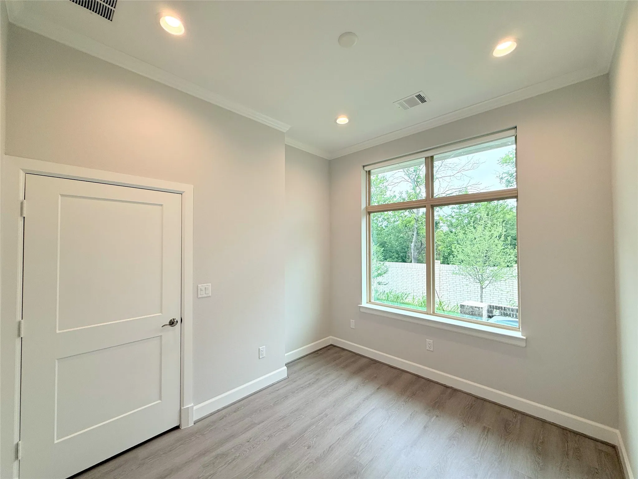 Room with a large multi-pane window, wood-finish flooring, recessed lighting, and crown molding
