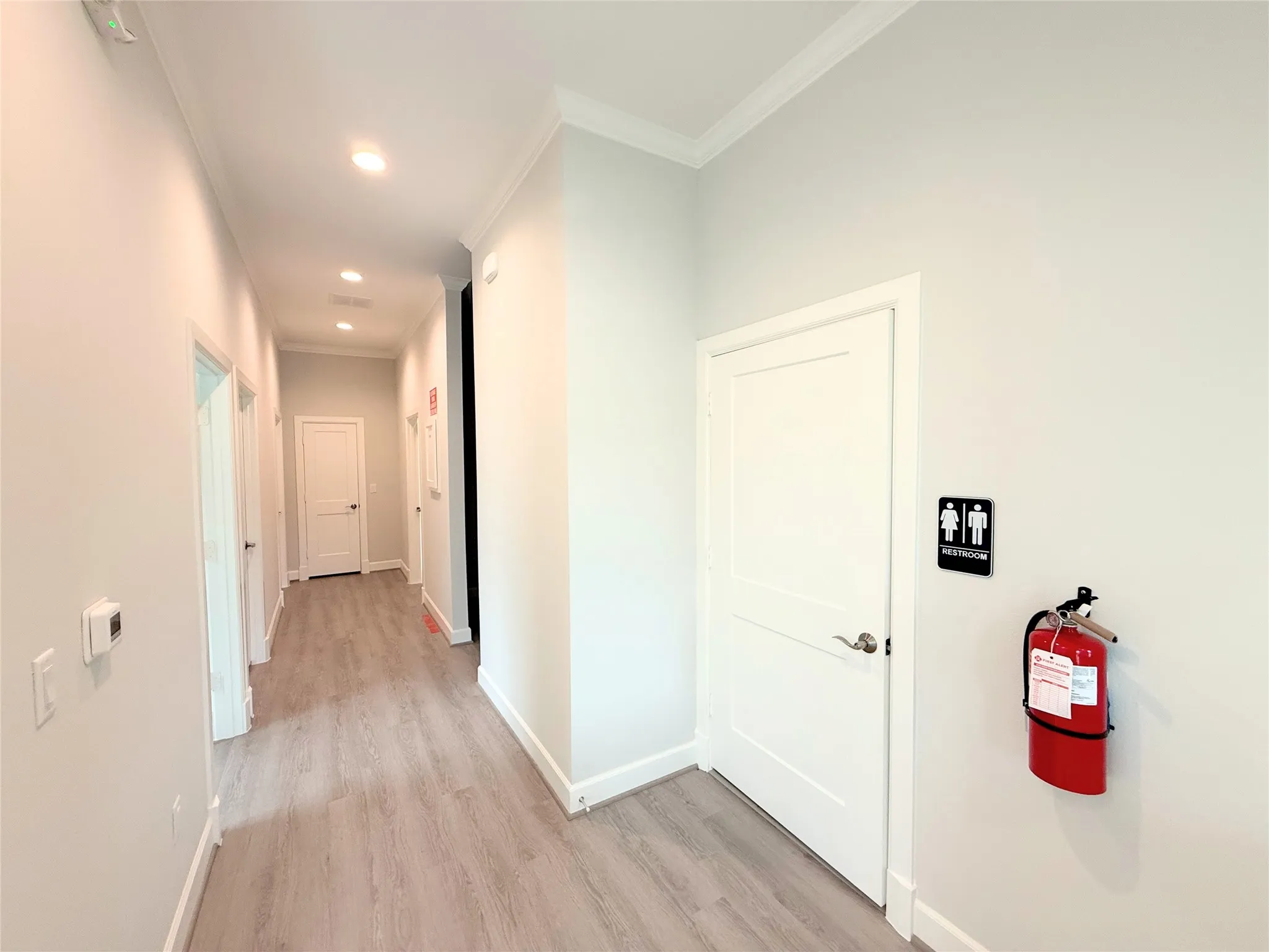 Hallway featuring light-toned wood-finish flooring, recessed ceiling lighting, crown molding, and white baseboards