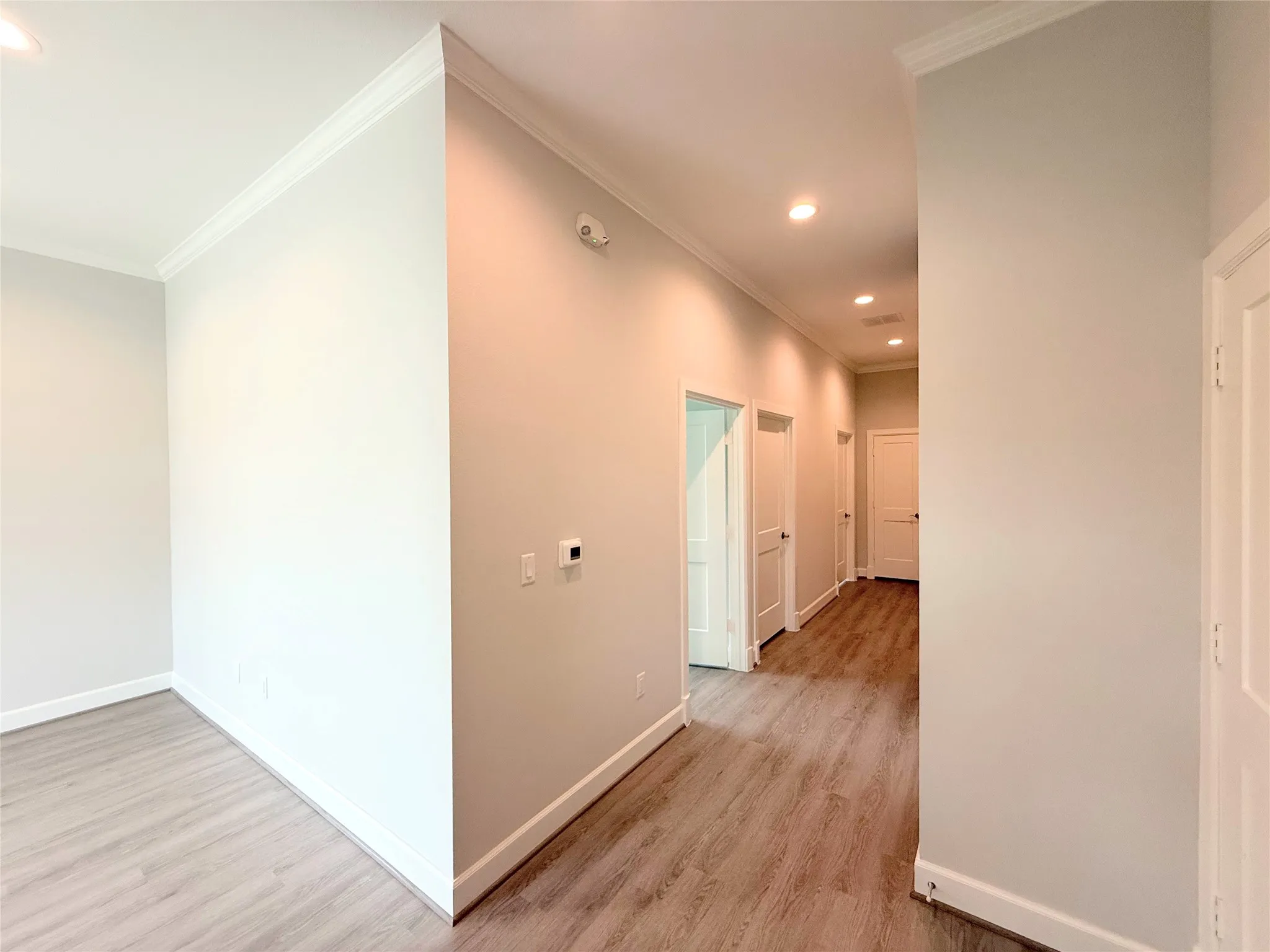 Hallway featuring recessed lighting, crown molding, wood-finish flooring, and white paneled doors