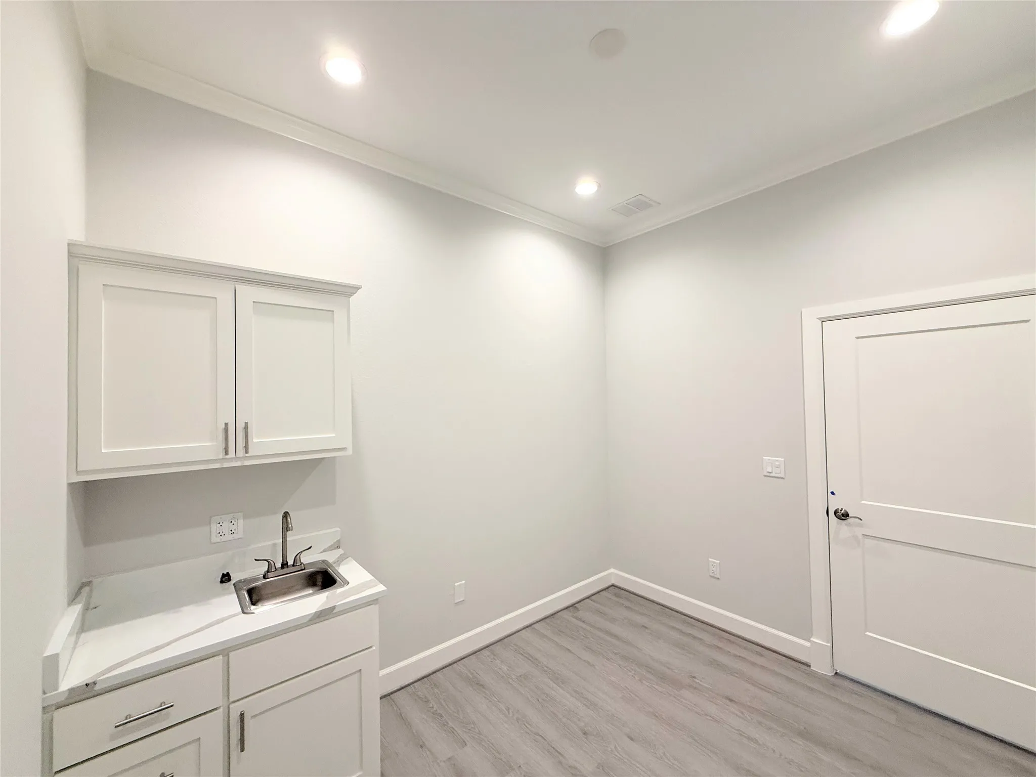 Utility space featuring a stainless steel sink, white shaker cabinetry with ample storage, a white countertop, and wood-finish flooring