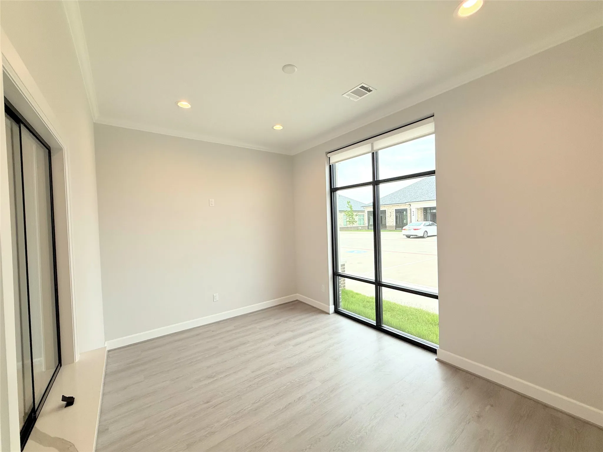 Room featuring a large picture window, recessed lighting, crown molding, light wood-finish flooring, and white baseboards