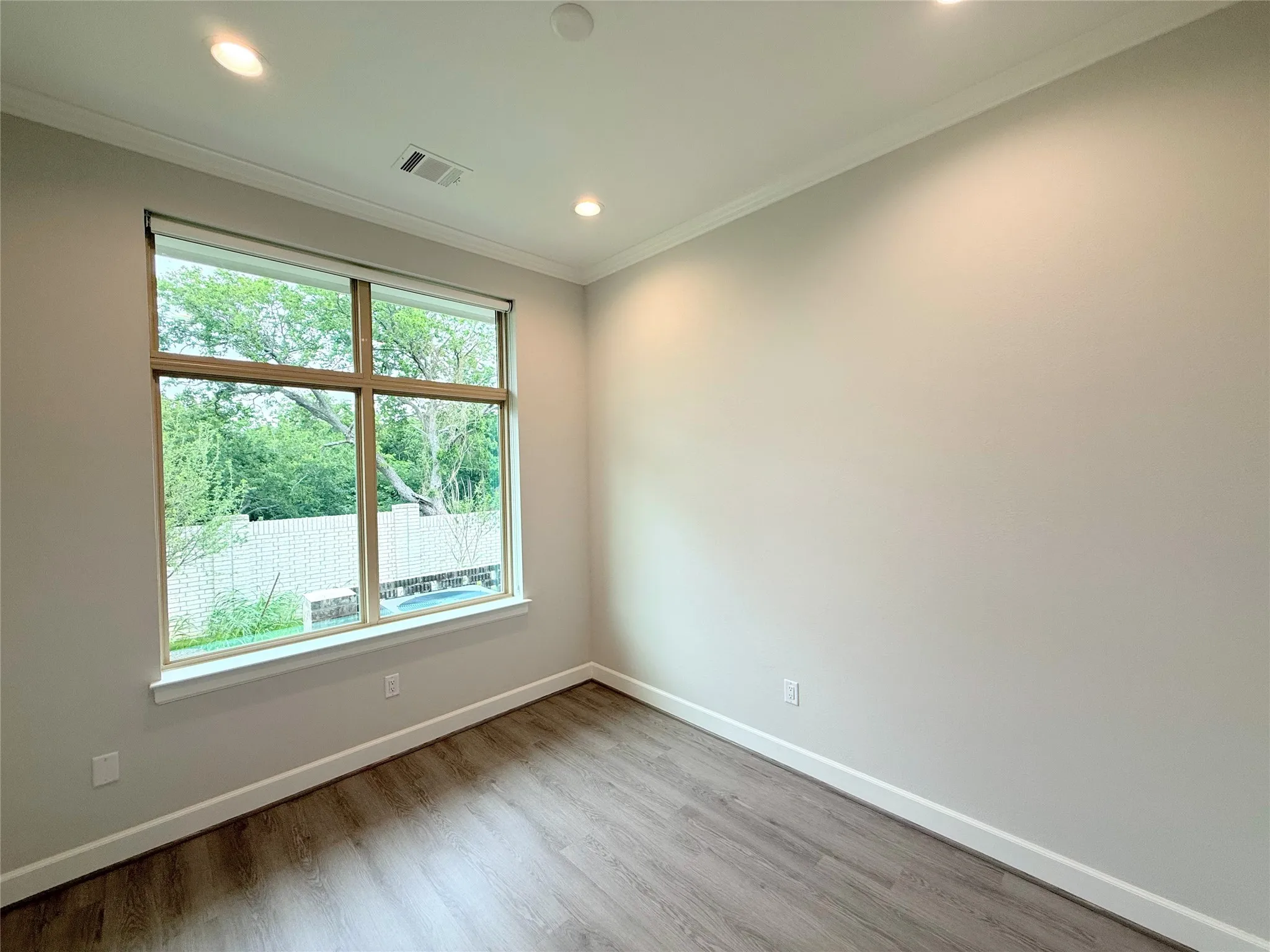 Room featuring a large window, wood-finish flooring, recessed lighting, crown molding, and painted walls