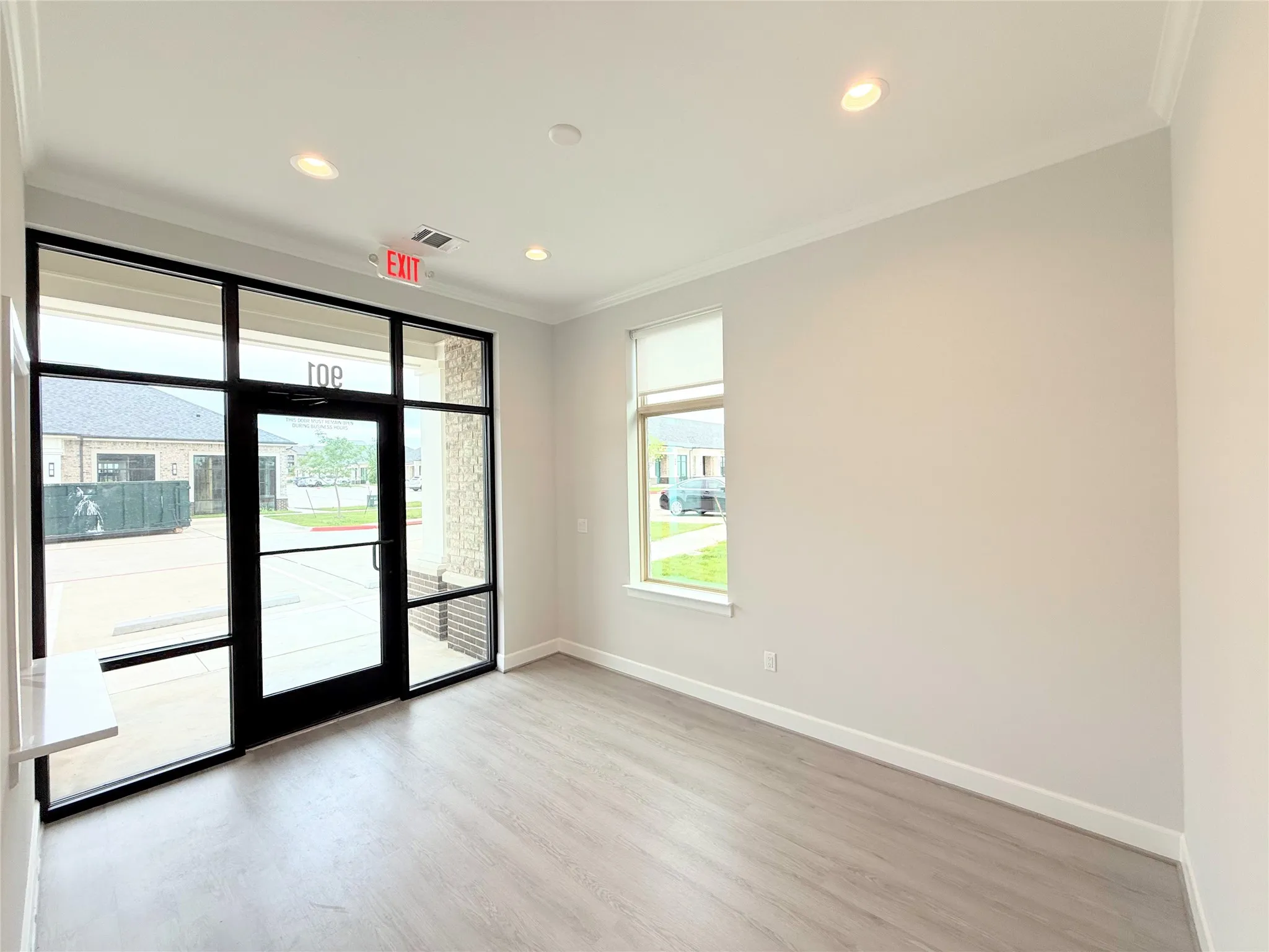 Entryway featuring a floor-to-ceiling glass storefront, black door frame, wood-finish flooring, recessed lighting, and a single window with a roller shade