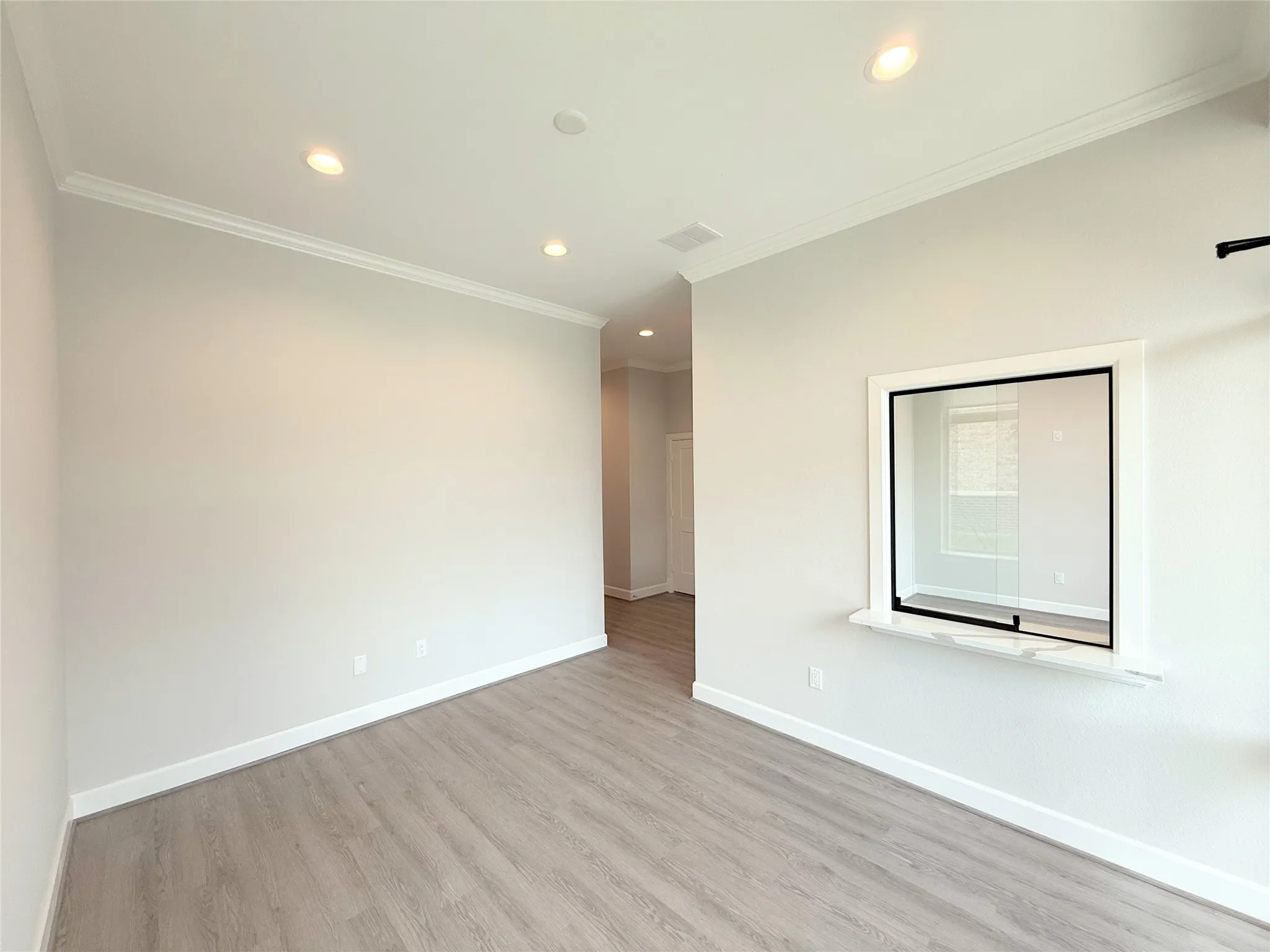 Spacious interior room featuring light-toned wood-finish flooring, recessed lighting, and crown molding